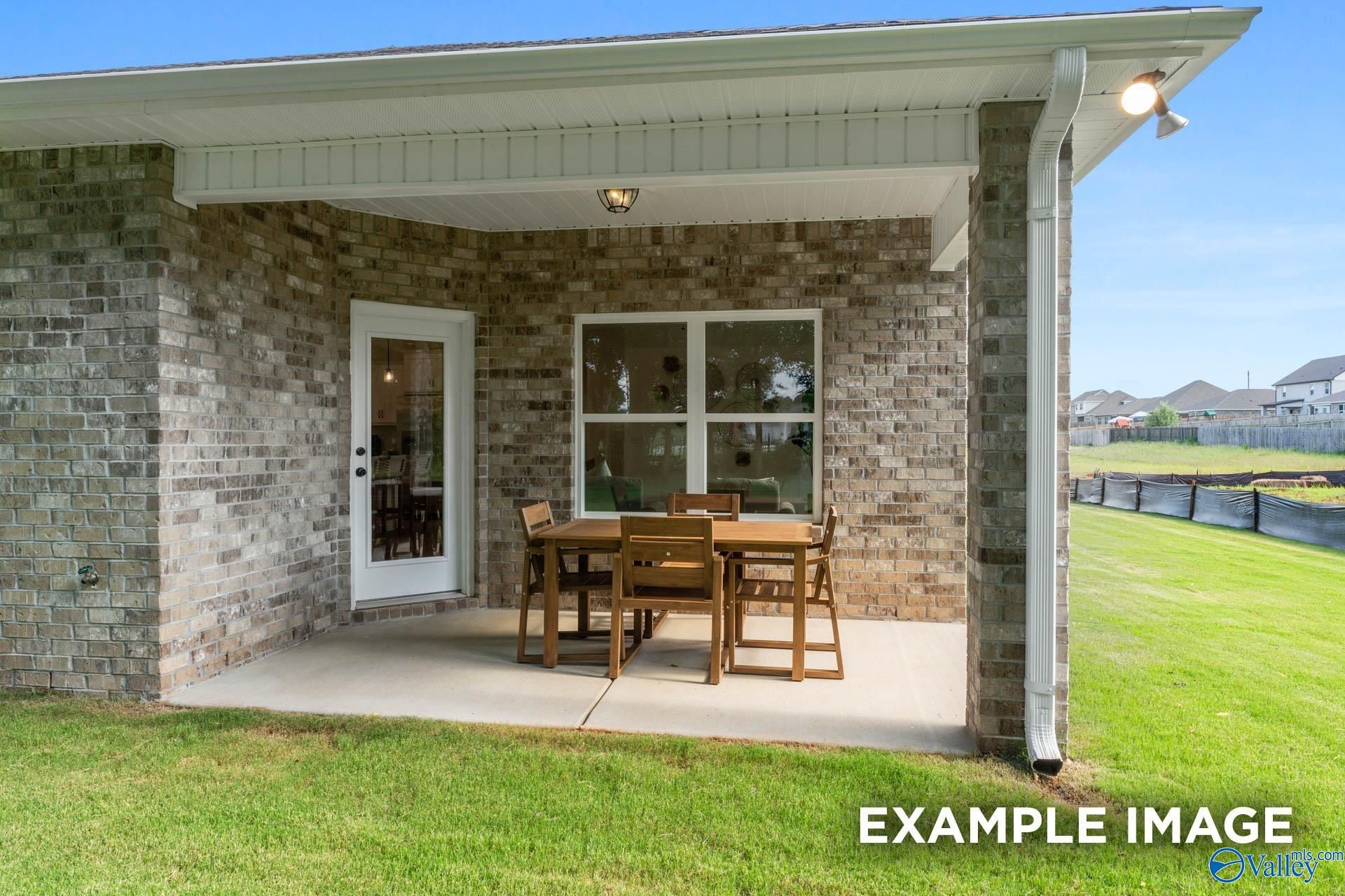Covered back patio with brick exterior, glass door, wooden dining table and chairs on concrete, green lawn view in The Franklin, Huntsville home