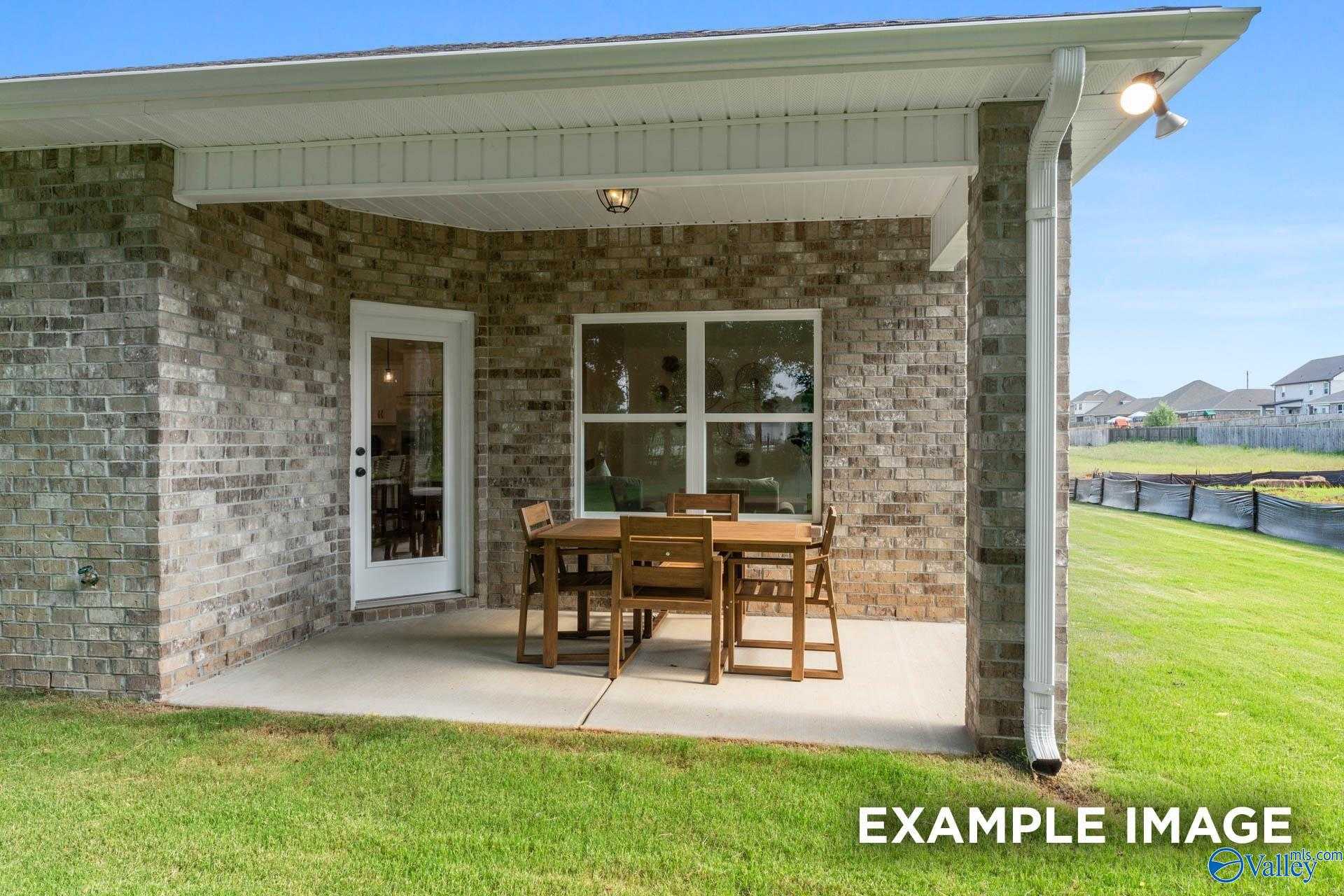 Covered back patio with wooden dining set on concrete slab, brick exterior, lush green yard in Davidson Homes The Franklin, Huntsville, Alabama