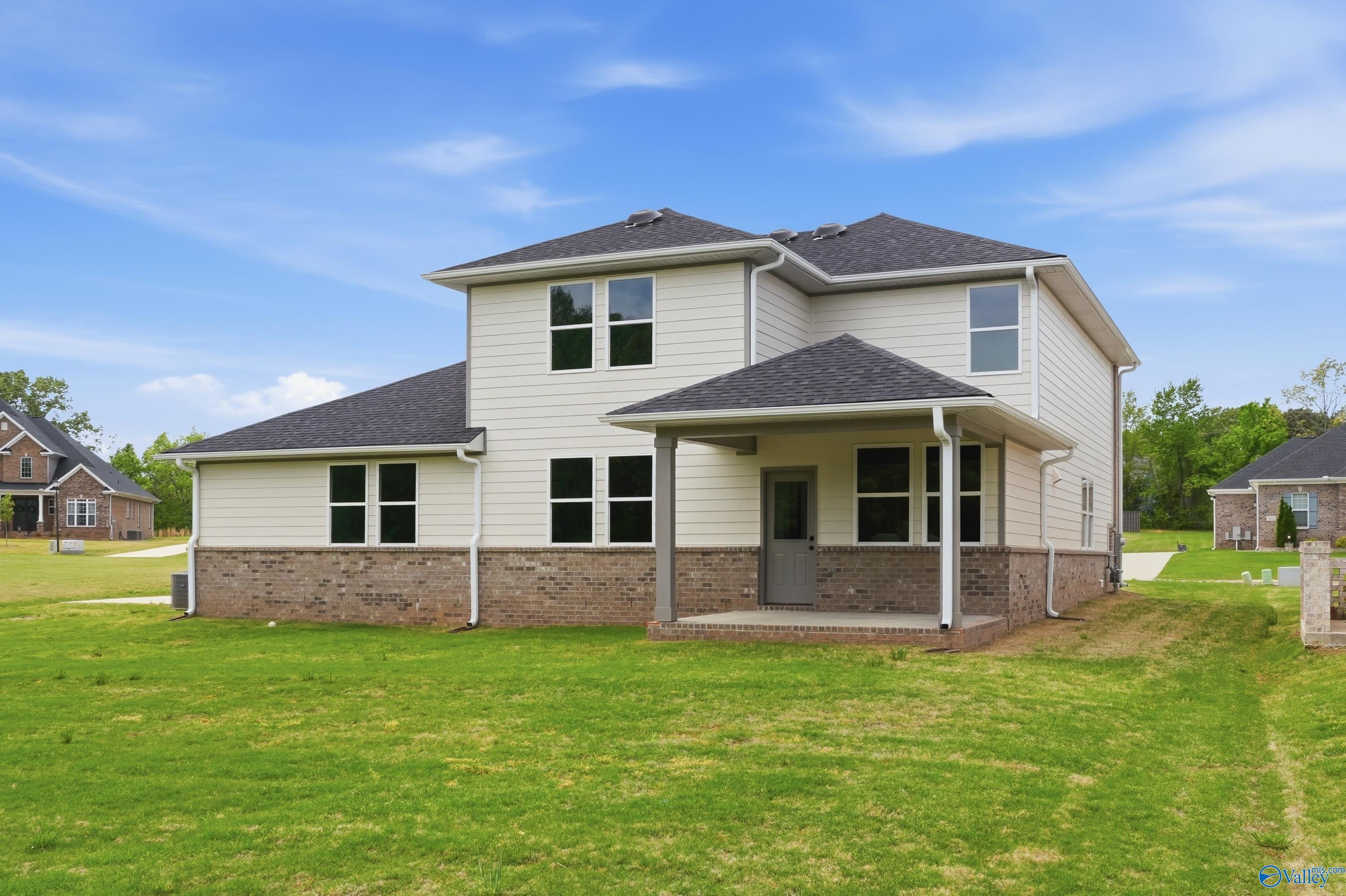 Two-story beige home with brick base, covered porch, large windows, and lush green lawn in Riverton Preserve, Huntsville, AL