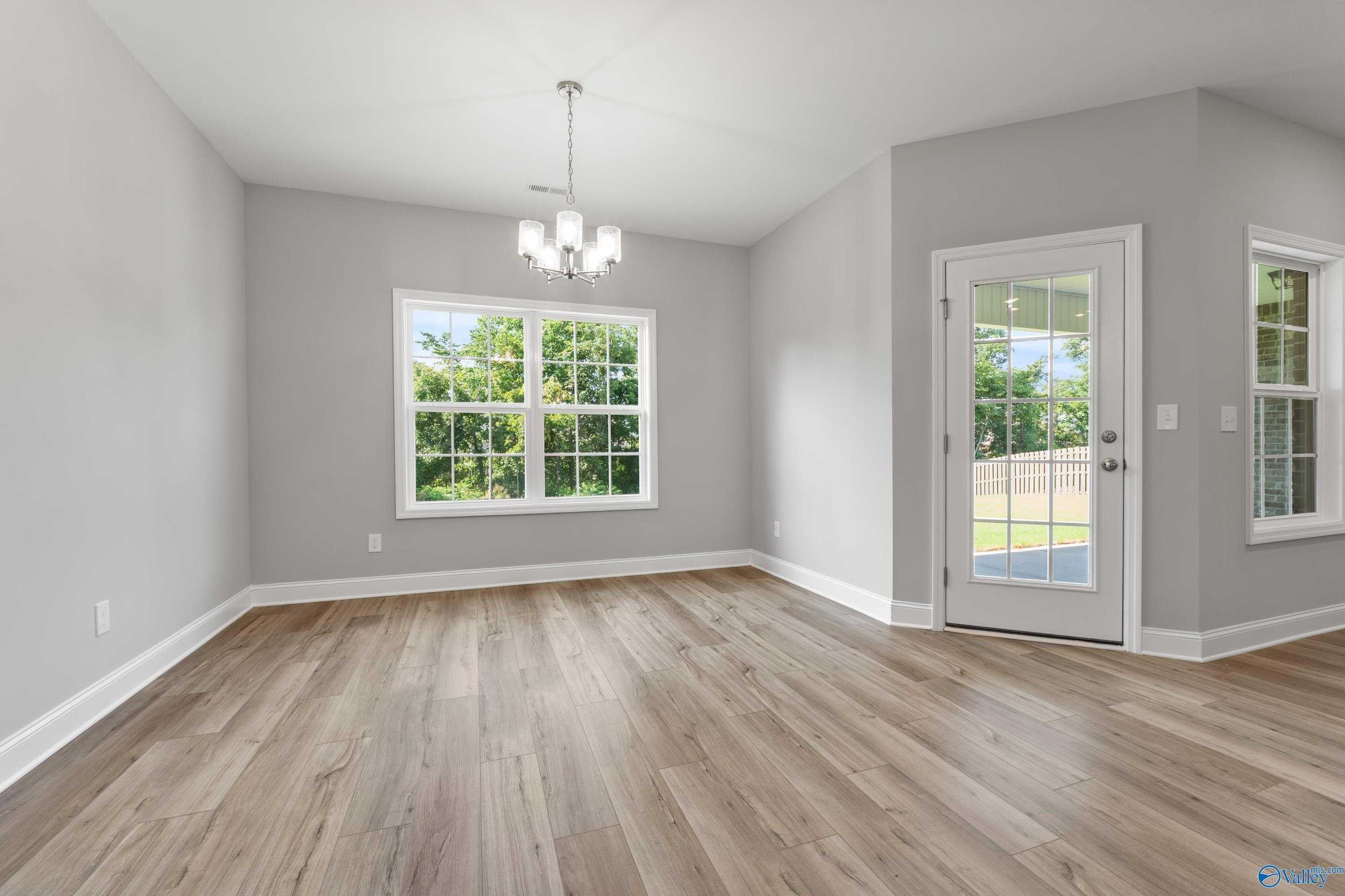 Bright dining room with gray walls, hardwood floors, chandelier, and large windows in Davidson Homes The Rockford, Harvest, AL