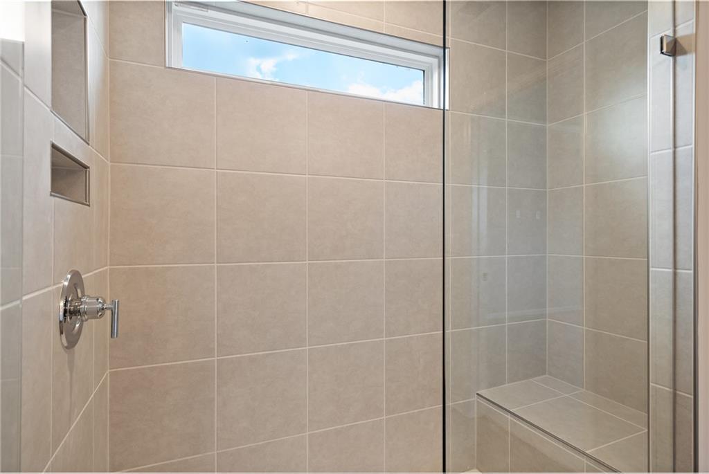 Modern tiled walk-in shower with glass enclosure, built-in bench, niche shelves and clerestory window in The Hickory A, Winder, Georgia