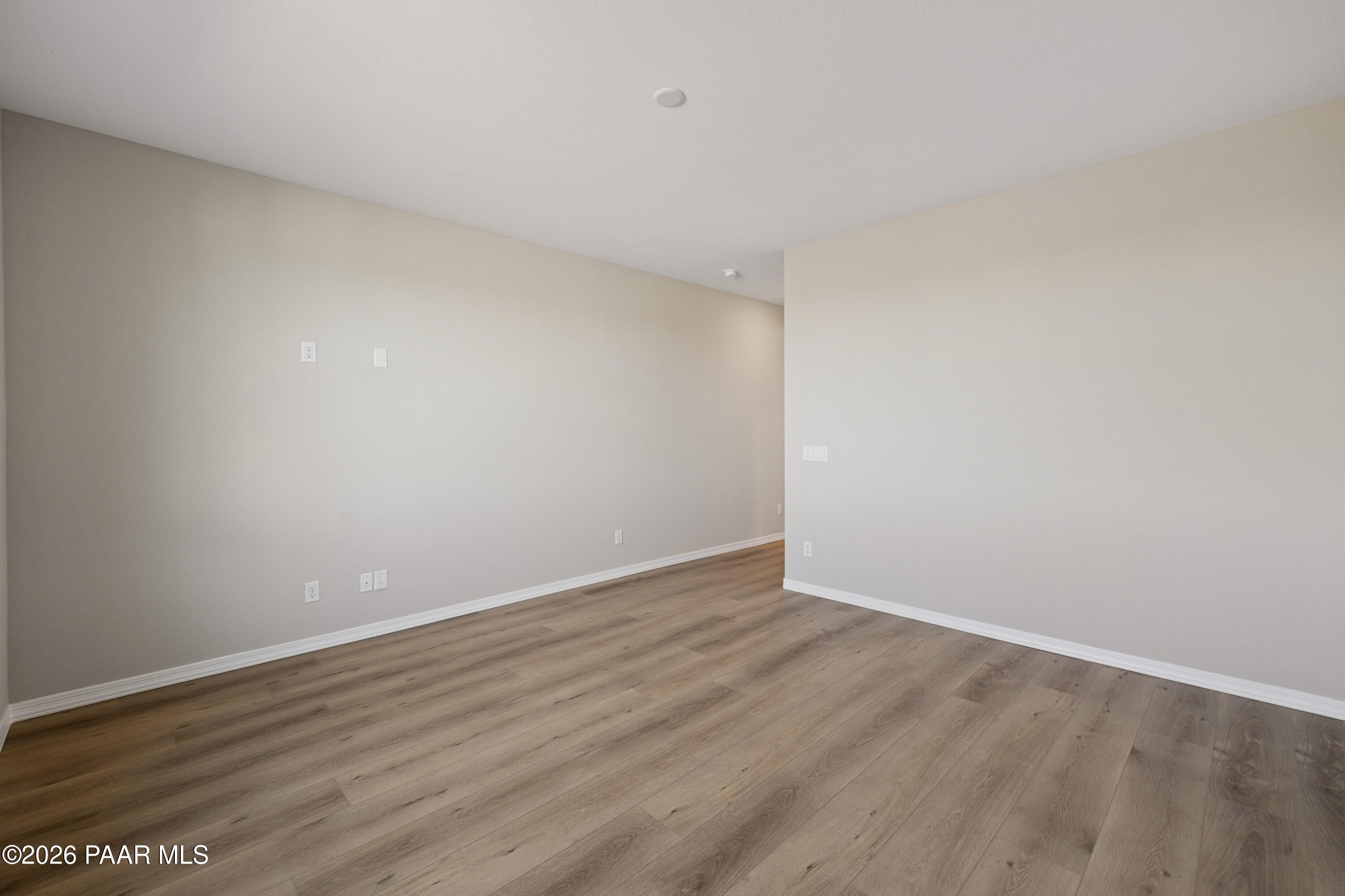 Spacious empty living area with light wood laminate floors and beige walls in Davidson Homes The Harmony A, Prescott Valley, AZ
