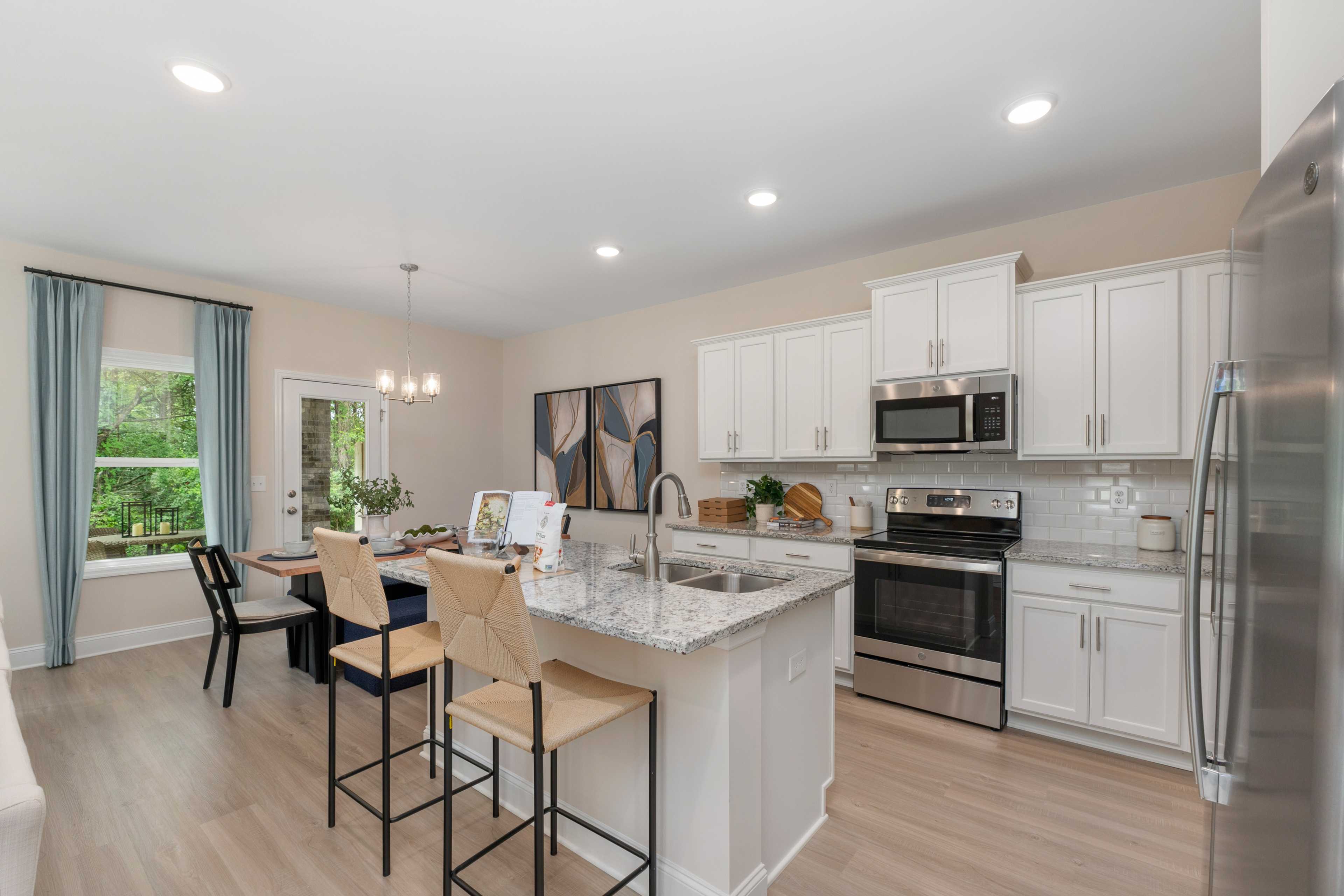 Spacious modern kitchen at Pavilion in Huntsville AL by Davidson Homes with white cabinets, quartz island, bar stools, stainless appliances and dining area