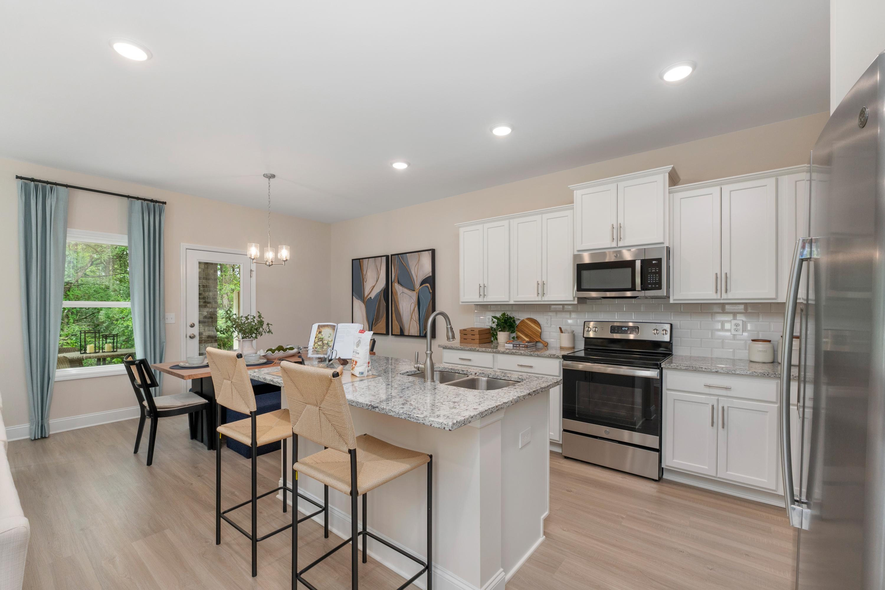 Spacious modern kitchen at Pavilion in Huntsville AL by Davidson Homes with white cabinets, quartz island, bar stools, stainless appliances and dining area