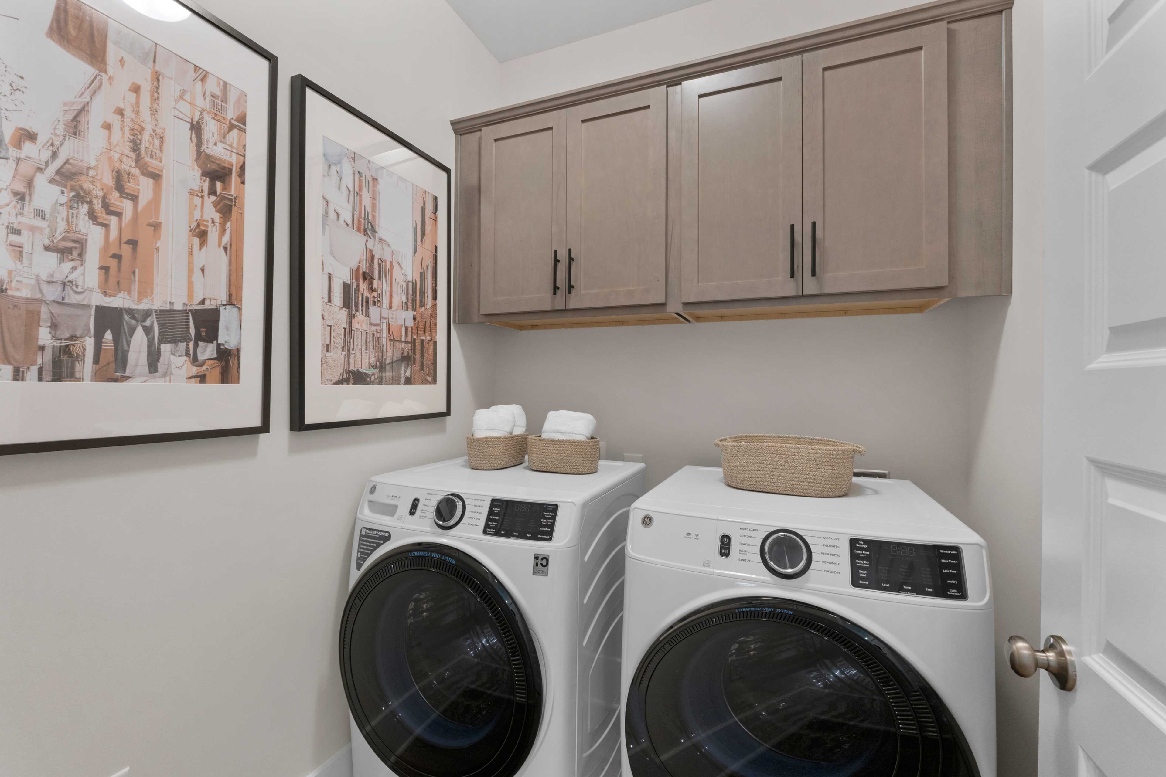 Spacious laundry room at Hollon Meadow in Decatur Alabama with front-load washers dryers beige cabinets and wall art