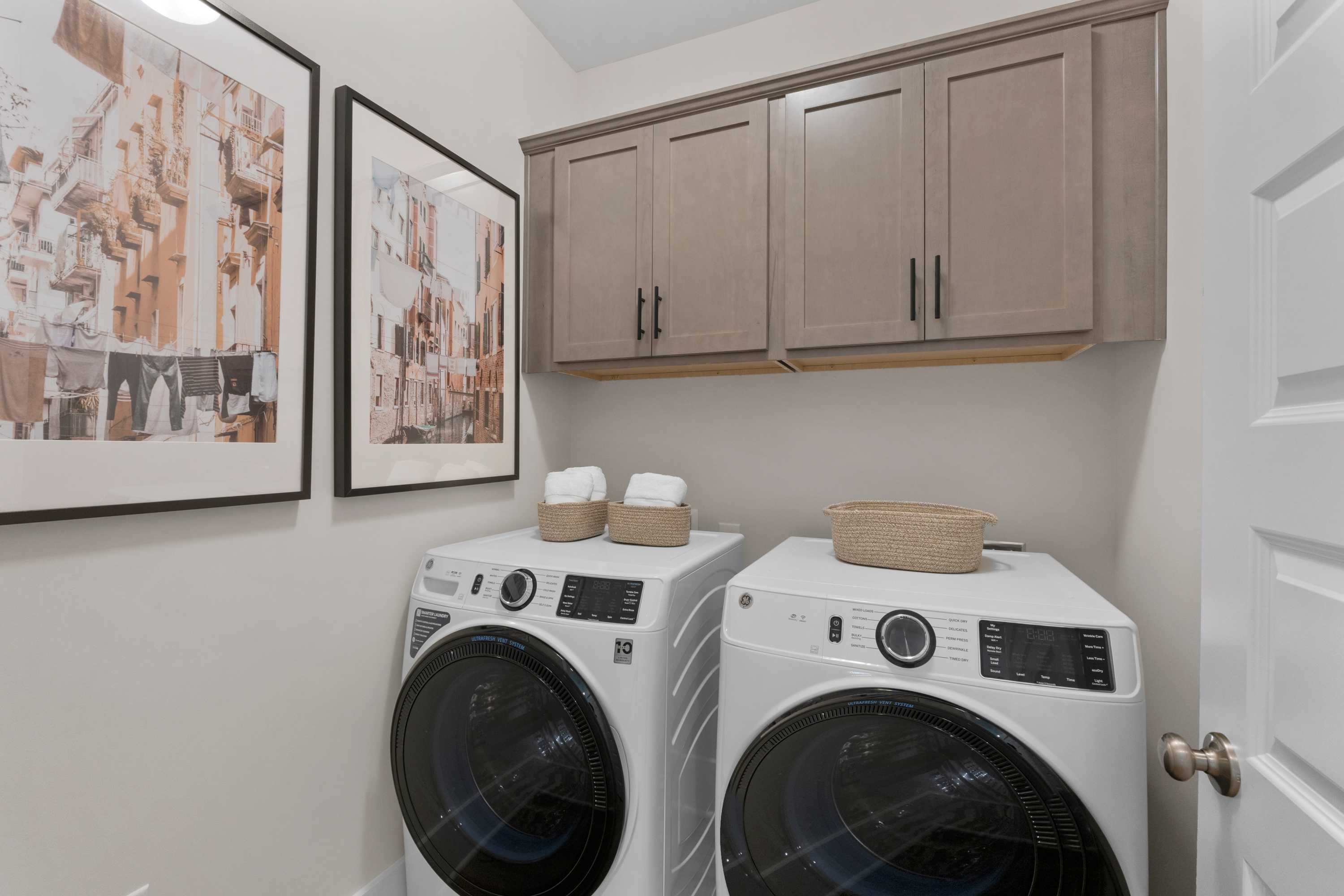 Spacious laundry room at Hollon Meadow in Decatur Alabama with front-load washers dryers beige cabinets and wall art