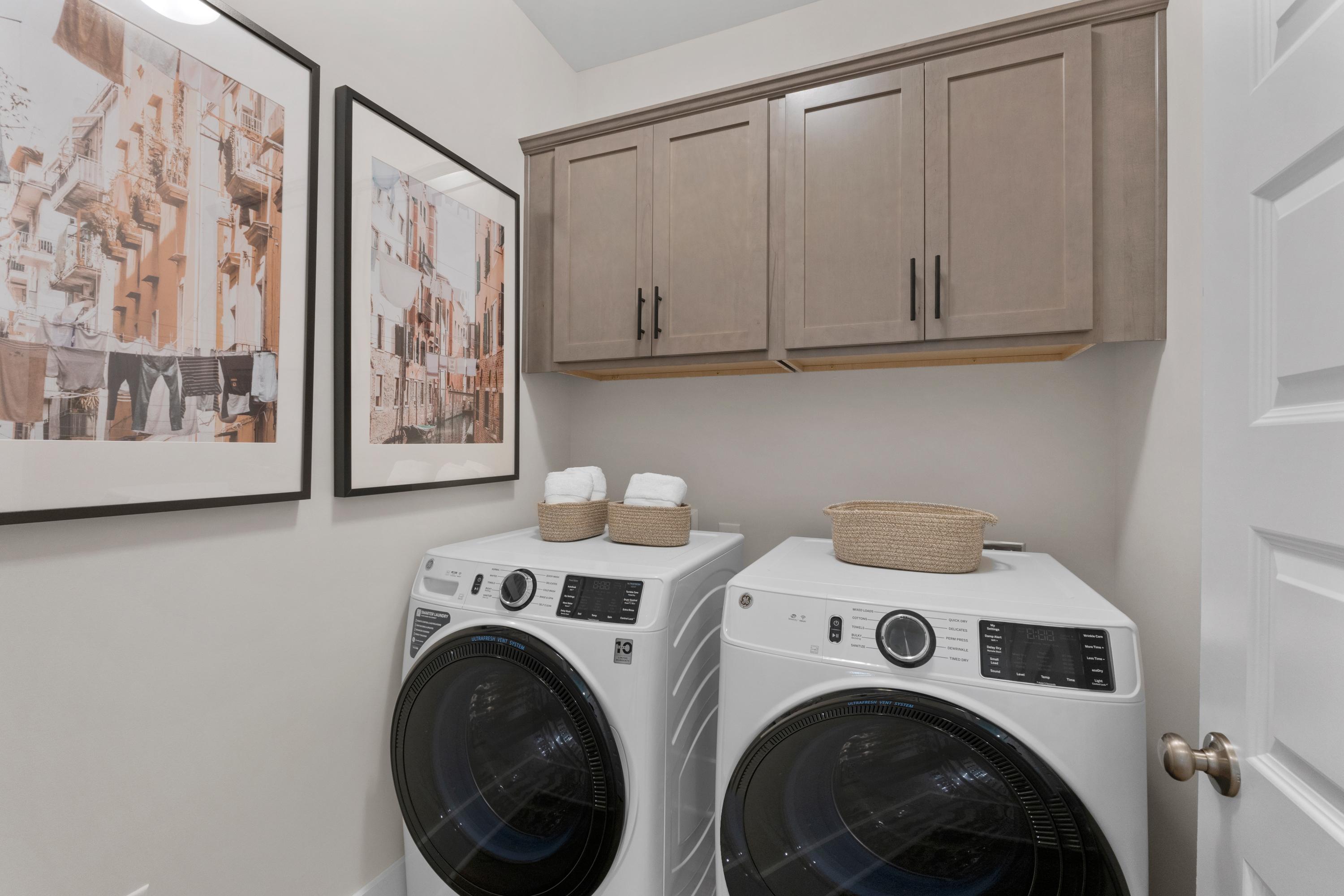 Spacious laundry room at Hollon Meadow in Decatur Alabama with front-load washers dryers beige cabinets and wall art