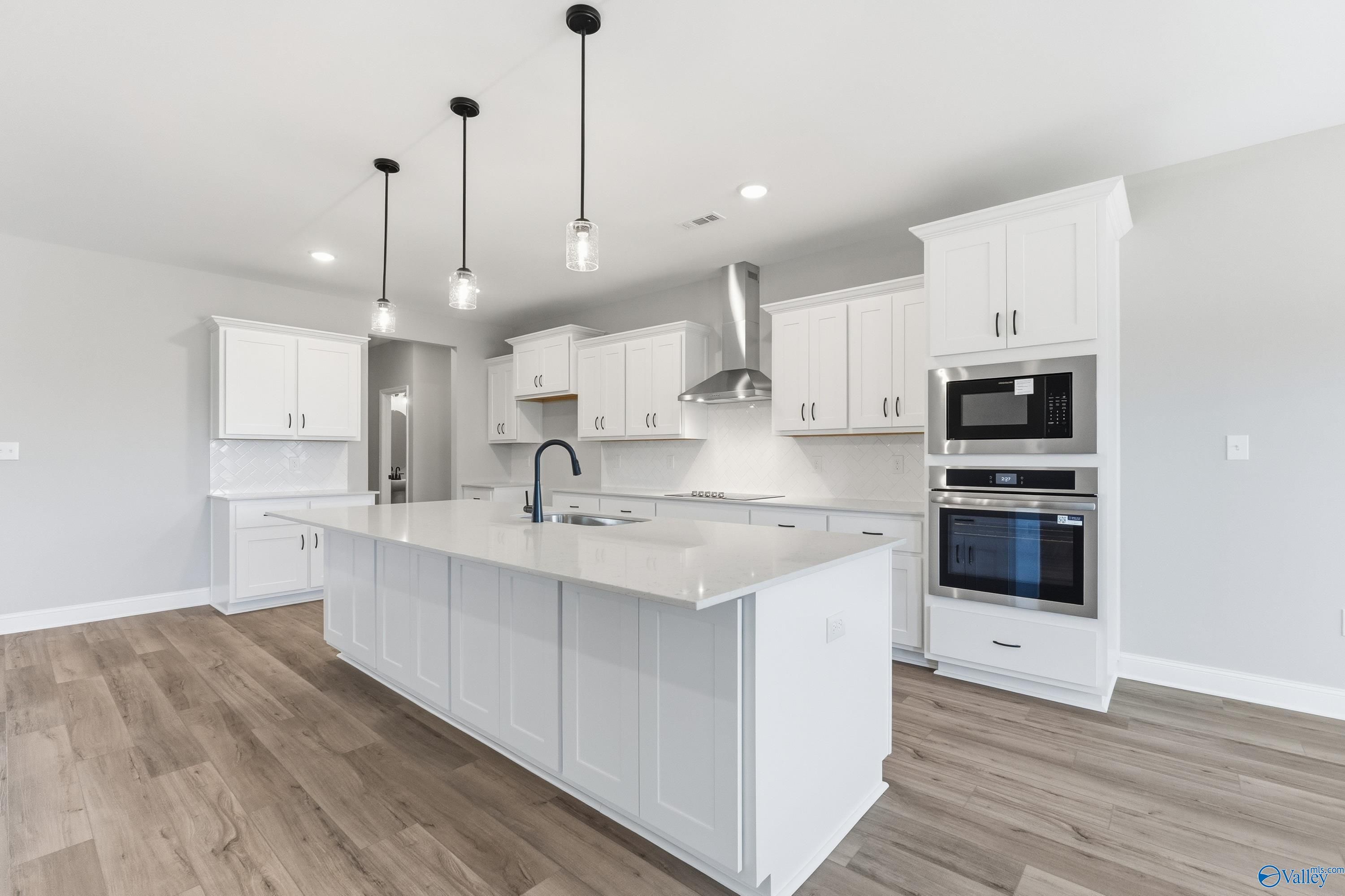 Modern white shaker kitchen with quartz island, stainless double oven, range hood, and pendant lights in The Finleigh by Davidson Homes, Meridianville, AL