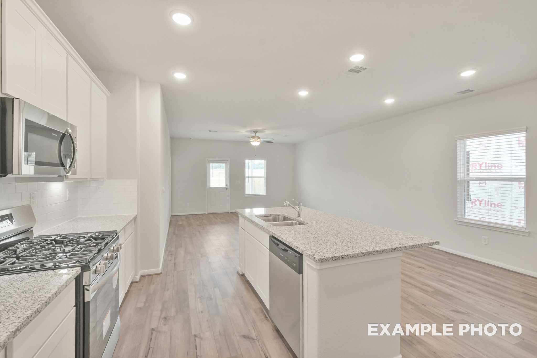 Open-concept kitchen and living area in The Brazos by Davidson Homes, featuring granite island, white cabinetry, and stainless appliances.