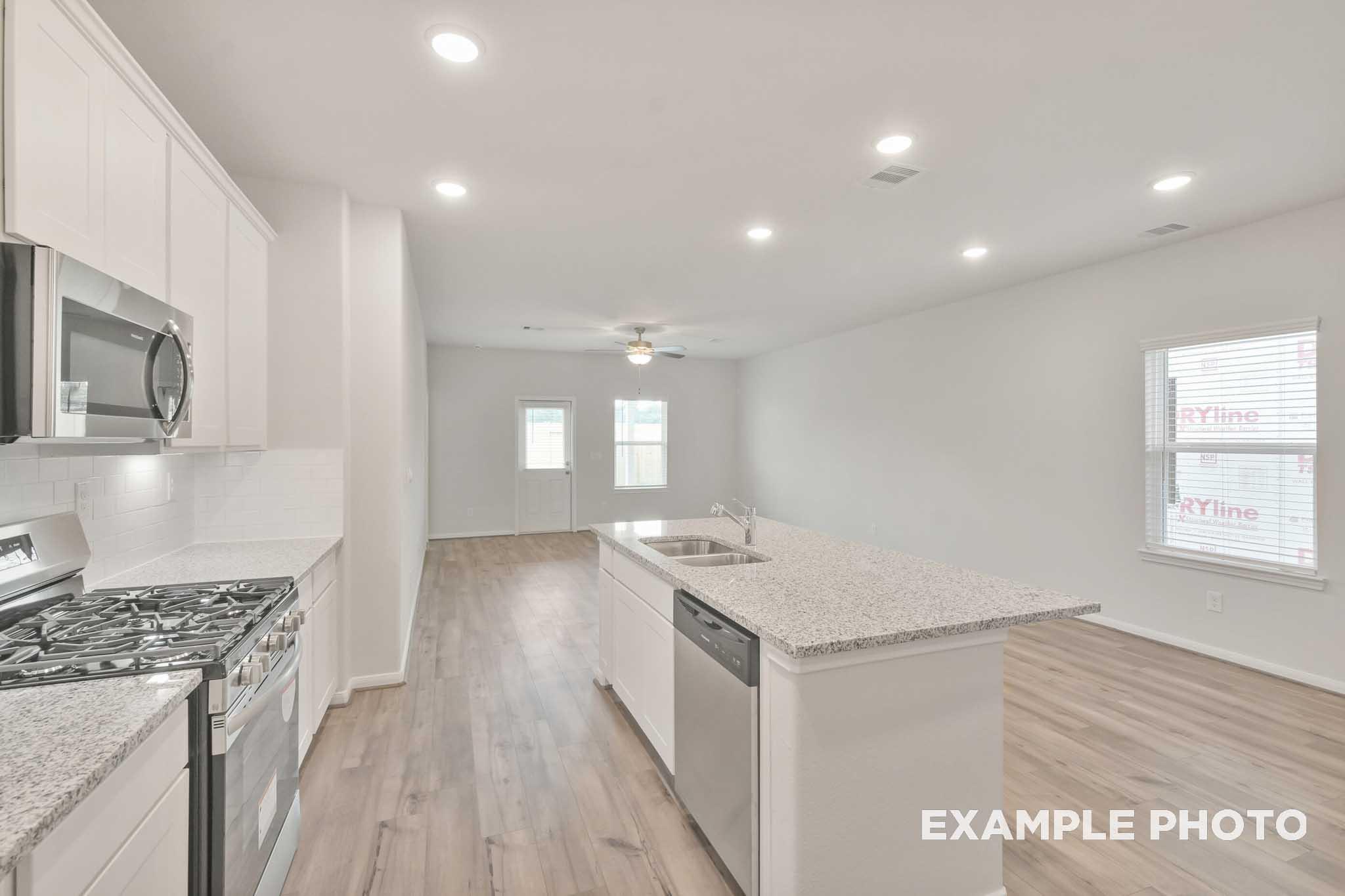 Open-concept kitchen and living area in The Brazos by Davidson Homes, featuring granite island, white cabinetry, and stainless appliances.