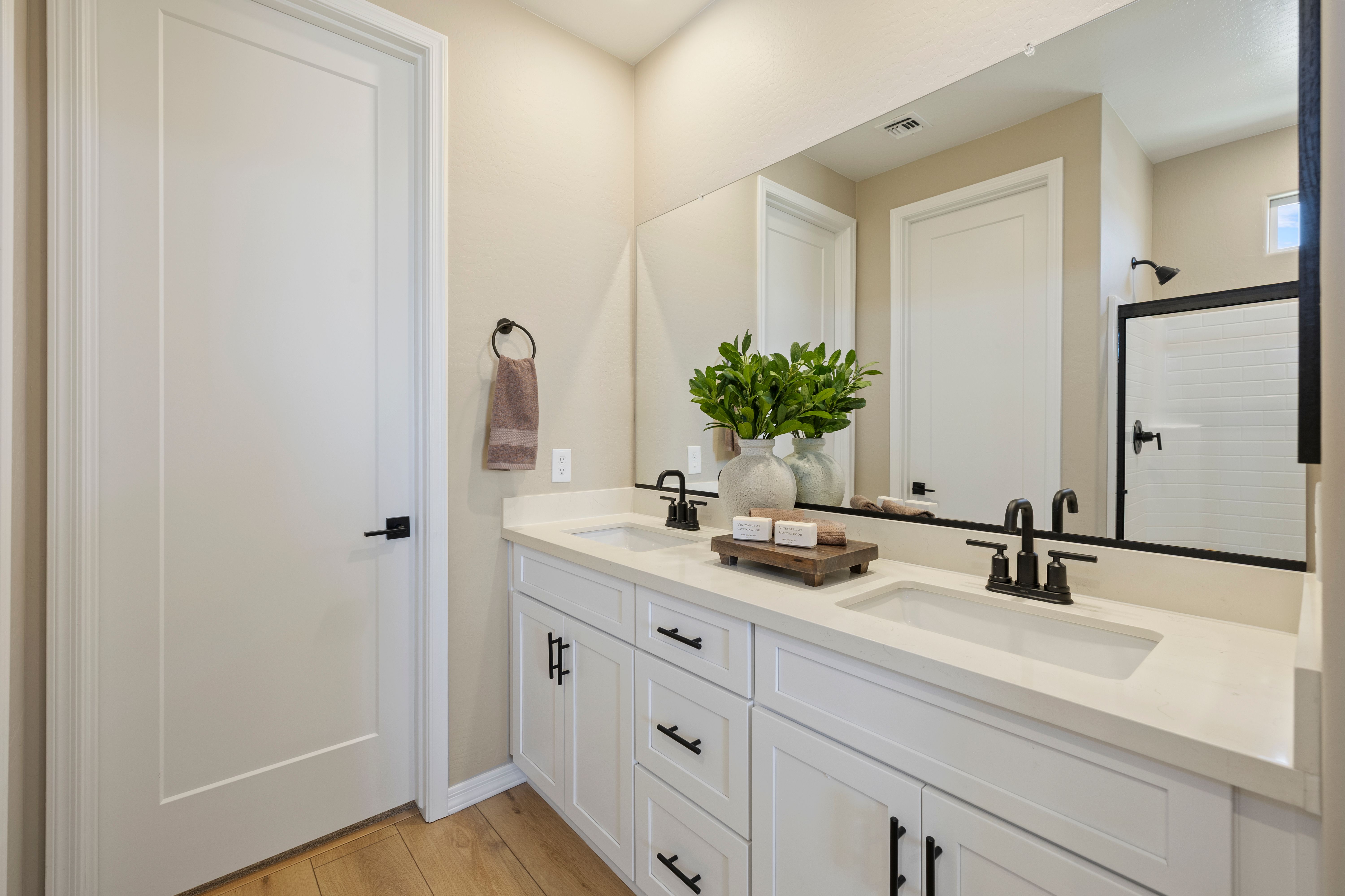 Modern primary bathroom at Vineyards at Cottonwood in Cottonwood AZ with double white vanity, quartz counters, black faucets, and walk-in shower