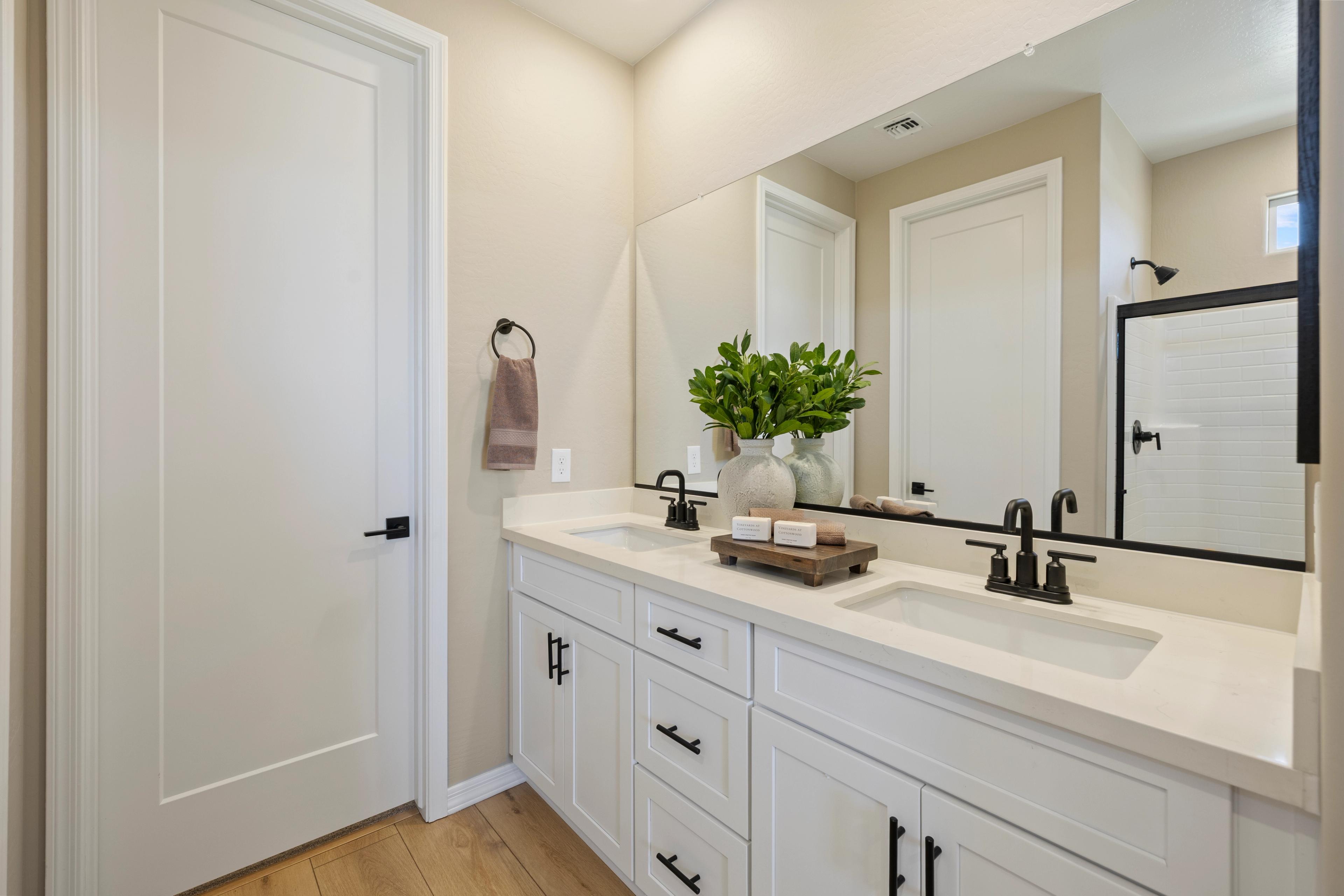 Modern primary bathroom at Vineyards at Cottonwood in Cottonwood AZ with double white vanity, quartz counters, black faucets, and walk-in shower