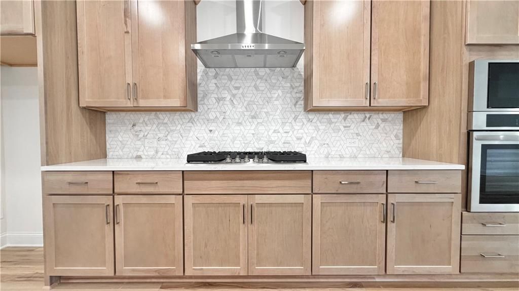 Modern kitchen with natural wood cabinets, gas cooktop, and geometric tile backsplash in The Glenwood A at Wehunt Meadows.
