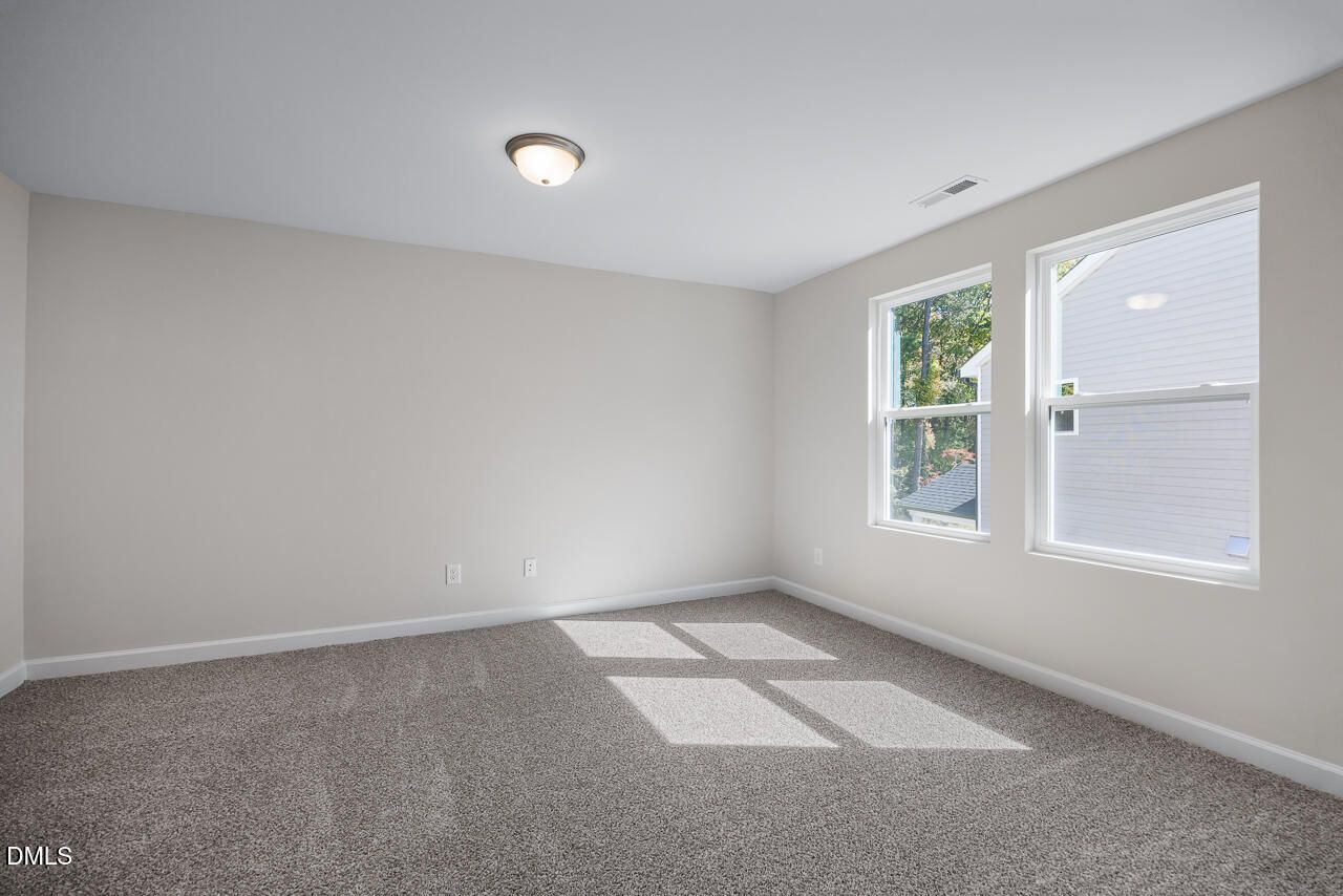 Bright empty bedroom with neutral gray walls, plush carpet, and large windows in Davidson Homes Grace C, Lillington, NC