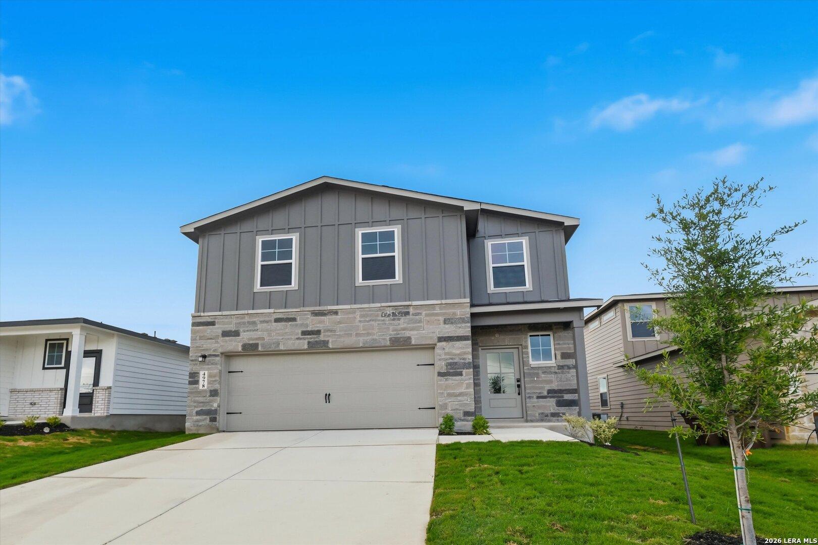 Modern two-story gray home with stone accents, 2-car garage, driveway, and lush green yard in Agave, San Antonio, Texas - Davidson Homes Blanco C