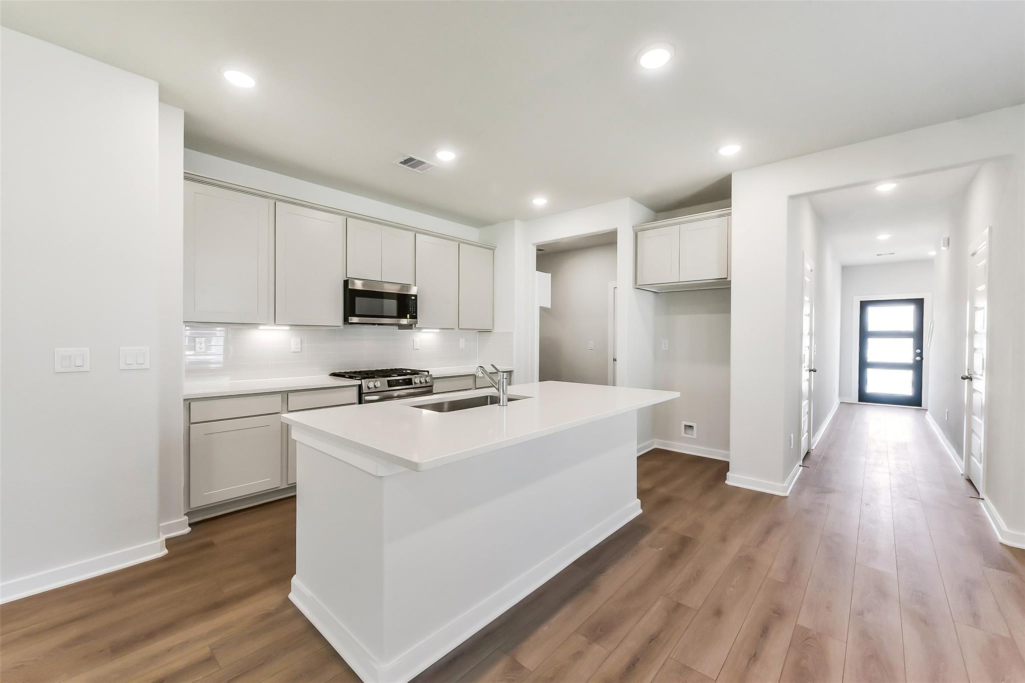 Bright modern kitchen with white island, stainless appliances, and open hallway in 5-bedroom Davidson Homes Brazos E, Magnolia Texas