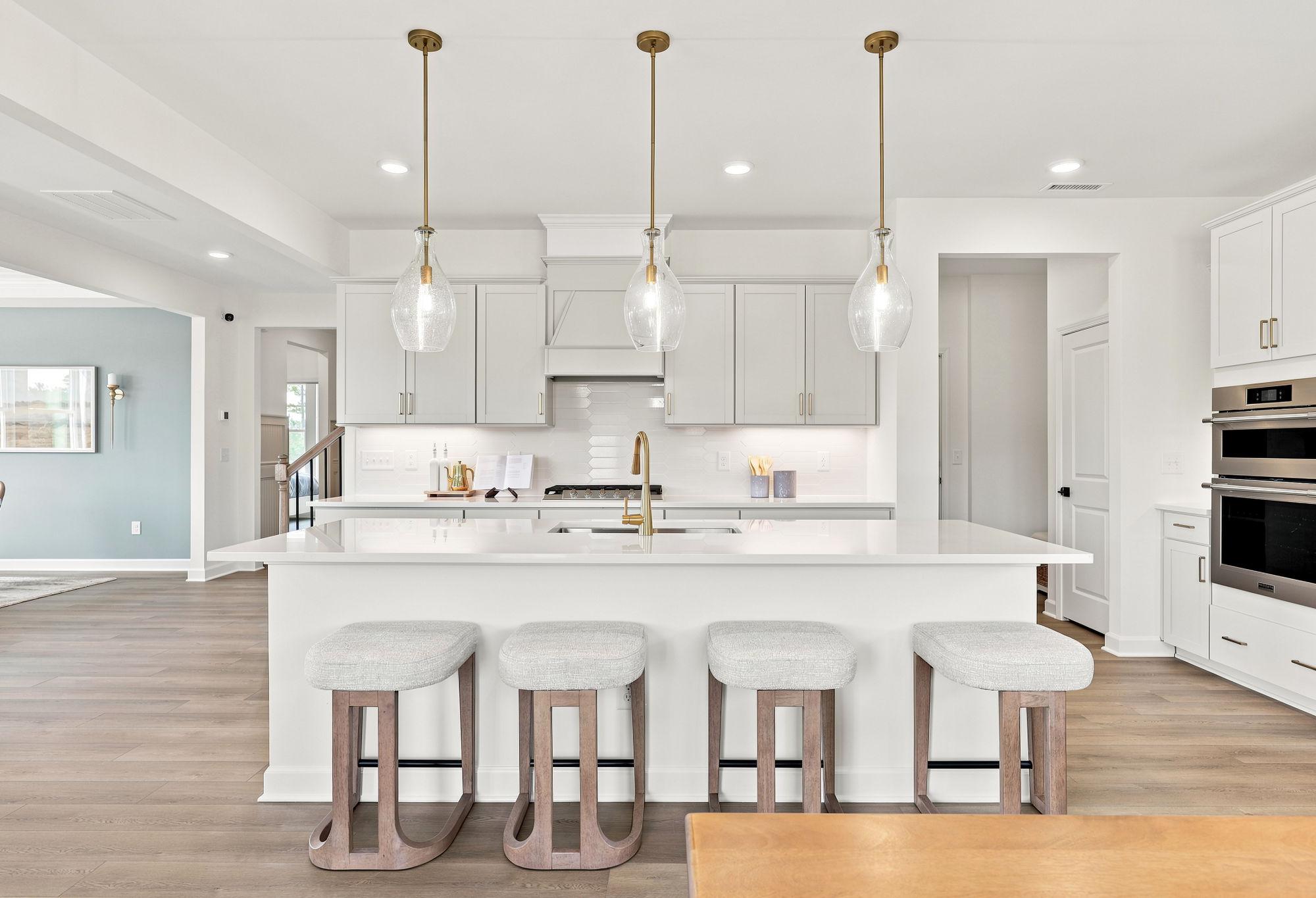 Modern gourmet kitchen in The Beech featuring a large white quartz island, pendant lighting, and stainless steel appliances.