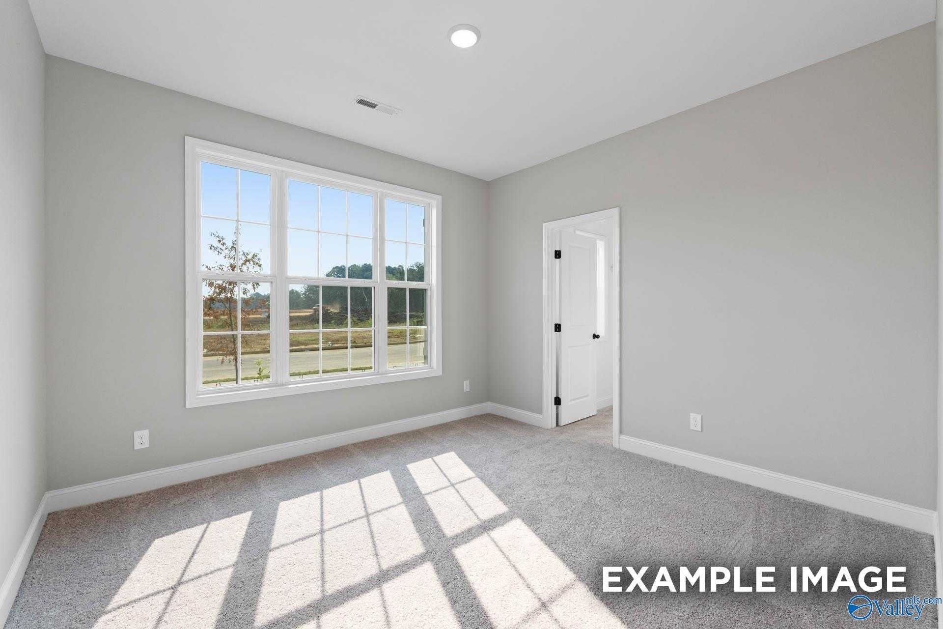 Bright bedroom with large bay window overlooking wooded yard, neutral gray walls, carpeted floor in The Montgomery B, Toney, AL