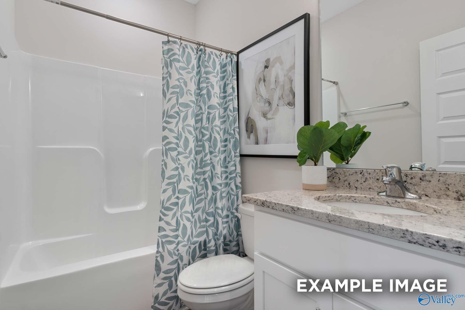 Bright bathroom with granite vanity, white cabinets, tub shower, and leaf-print curtain in Davidson Homes Camilla C plan