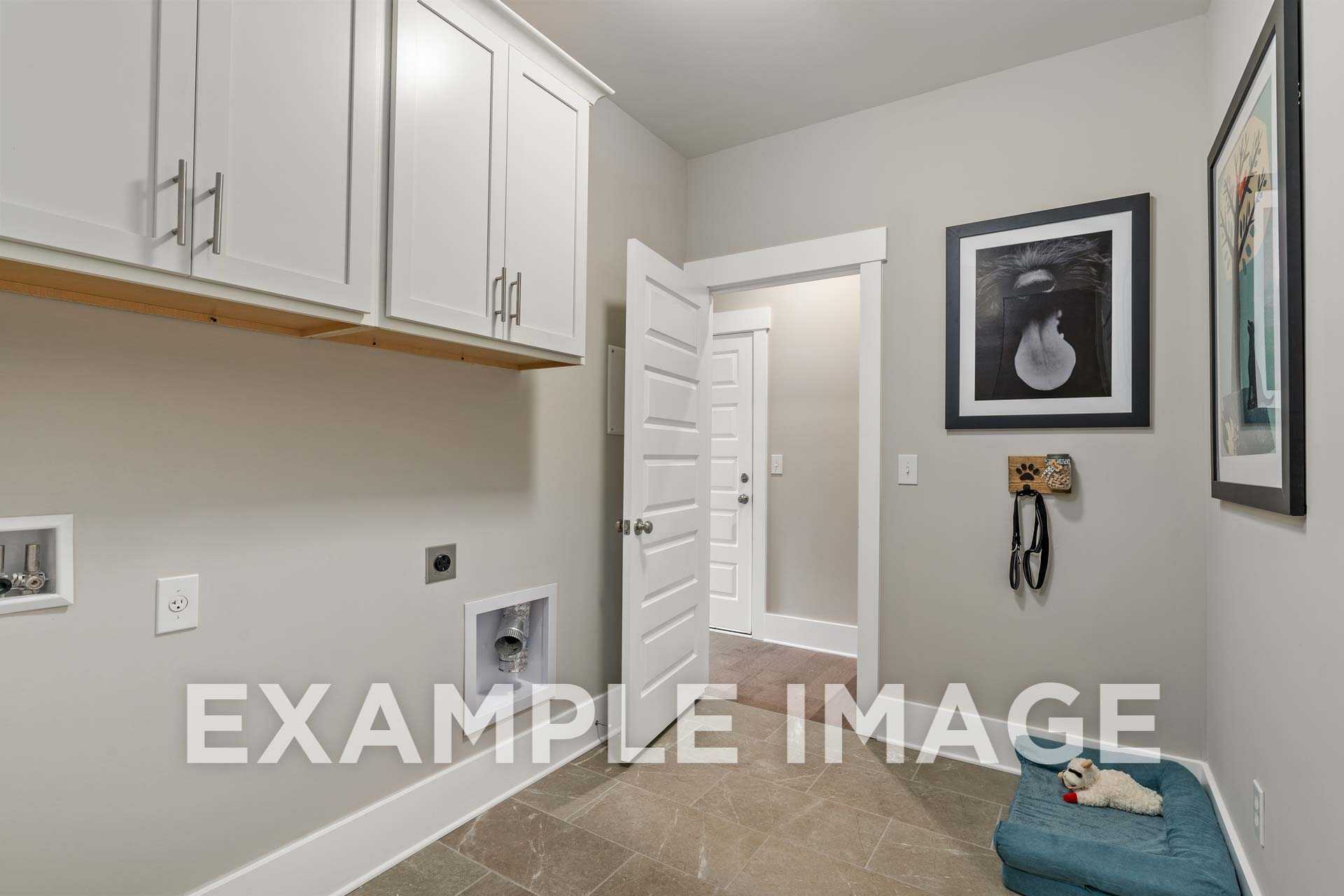 Spacious laundry room in The Harrison home with white cabinets, washer dryer hookups, and dog bed