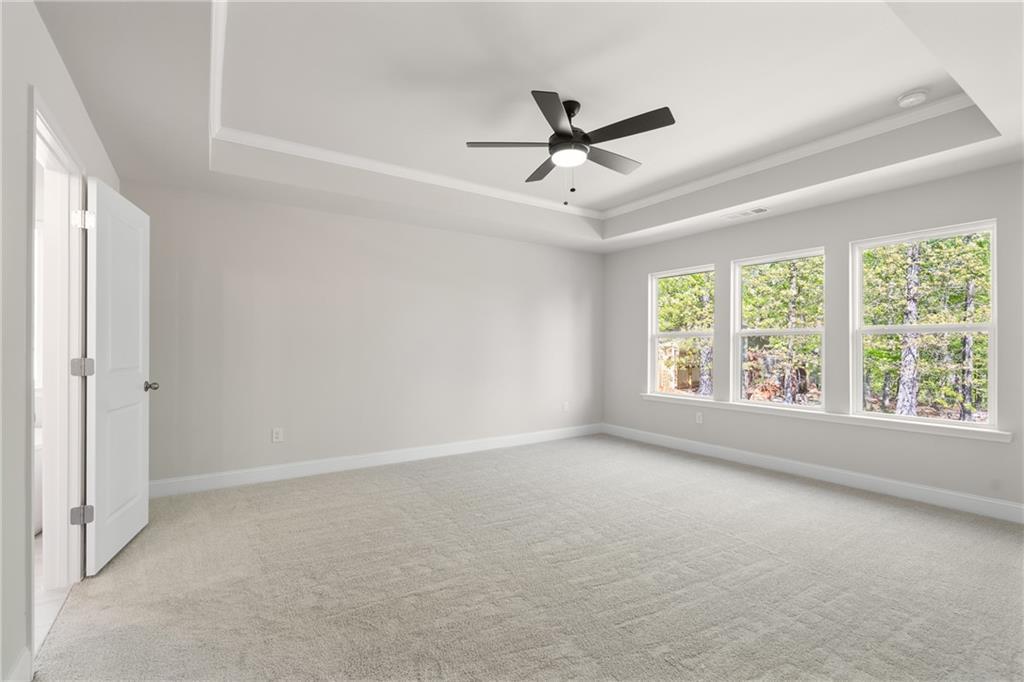 Spacious empty bedroom featuring tray ceiling, ceiling fan, large wooded-view windows in Davidson Homes The Hickory E, Buford, GA