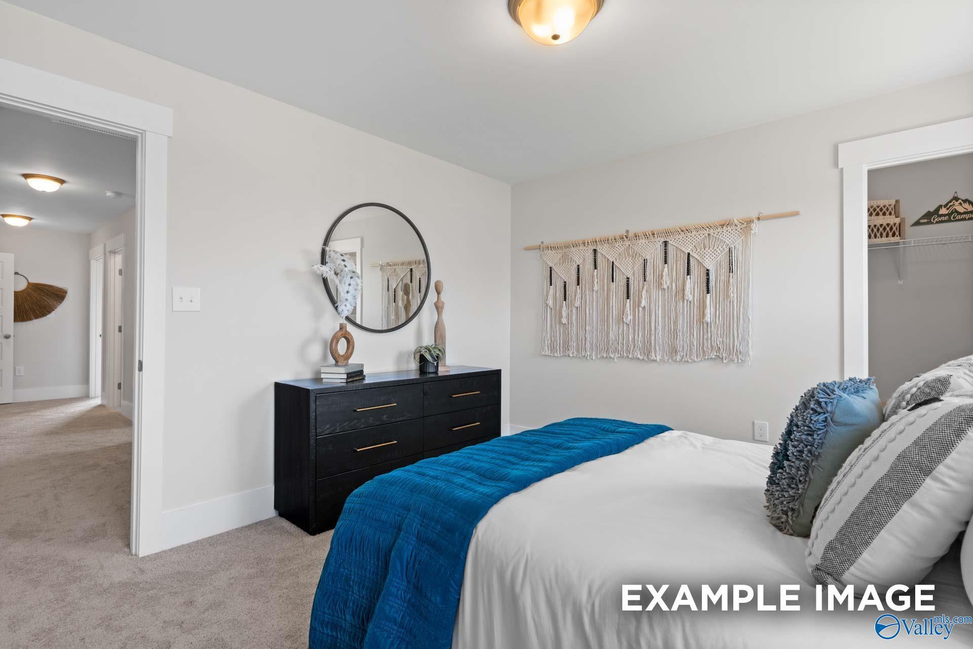 Cozy bedroom with blue accent bedding, black dresser, and macrame wall art in Davidson Homes' The Chelsea A, Ivy Hills, Toney, Alabama