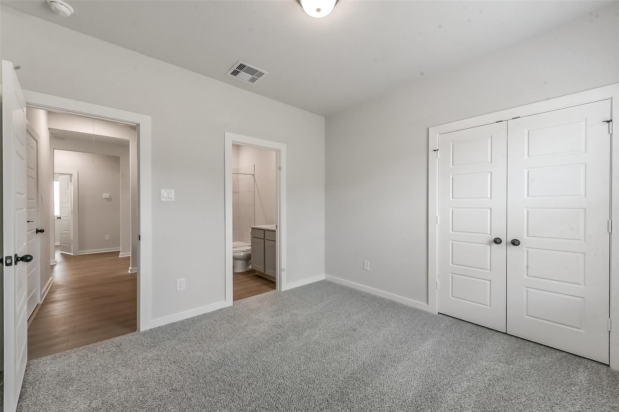 Bright bedroom with gray carpet, attached bath featuring shower and vanity, double closet doors in Davidson Homes The Everett C, Crosby Texas