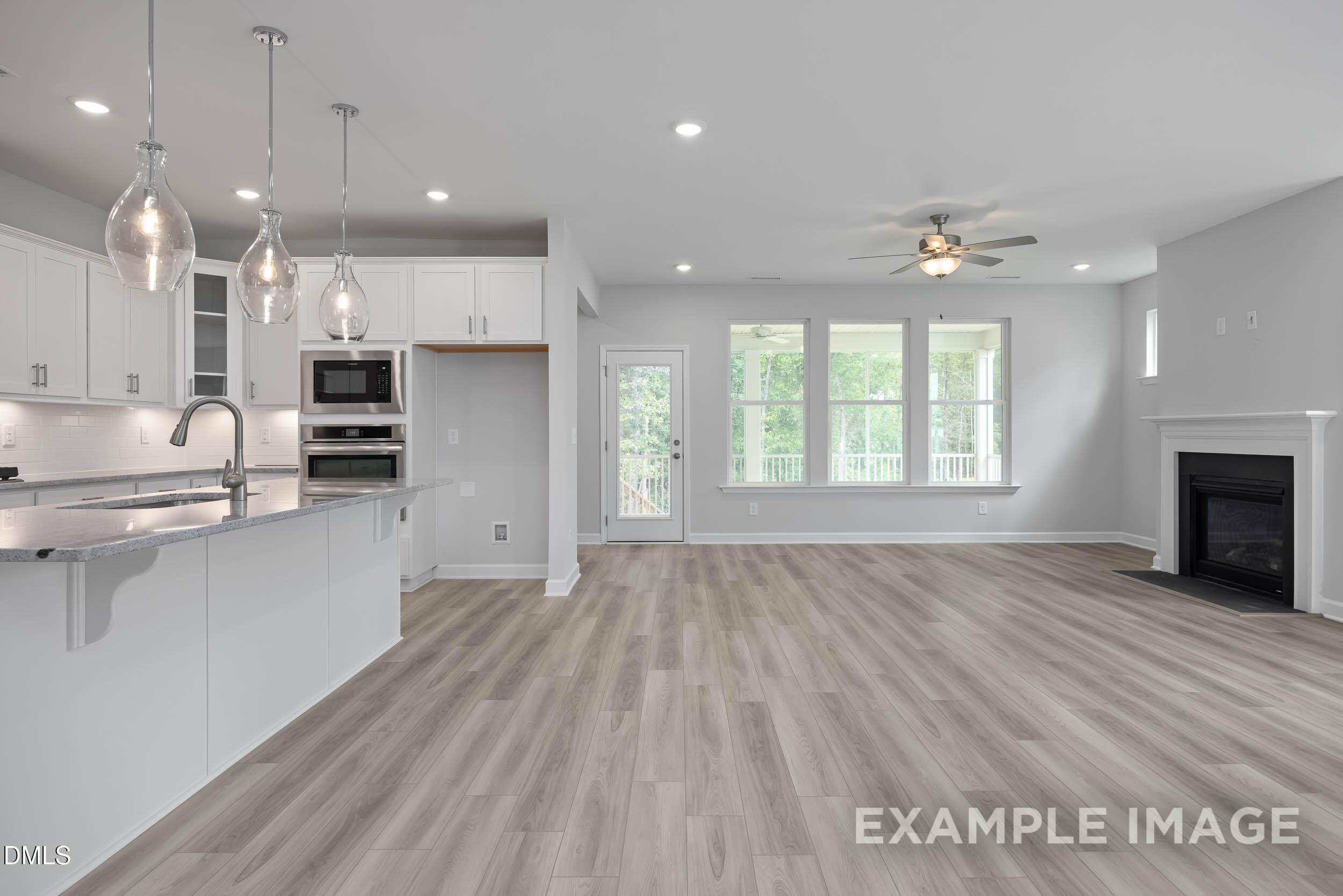Open-concept kitchen and great room with white cabinets, large island, fireplace, and natural light in The Magnolia B by Davidson Homes, Lillington, NC