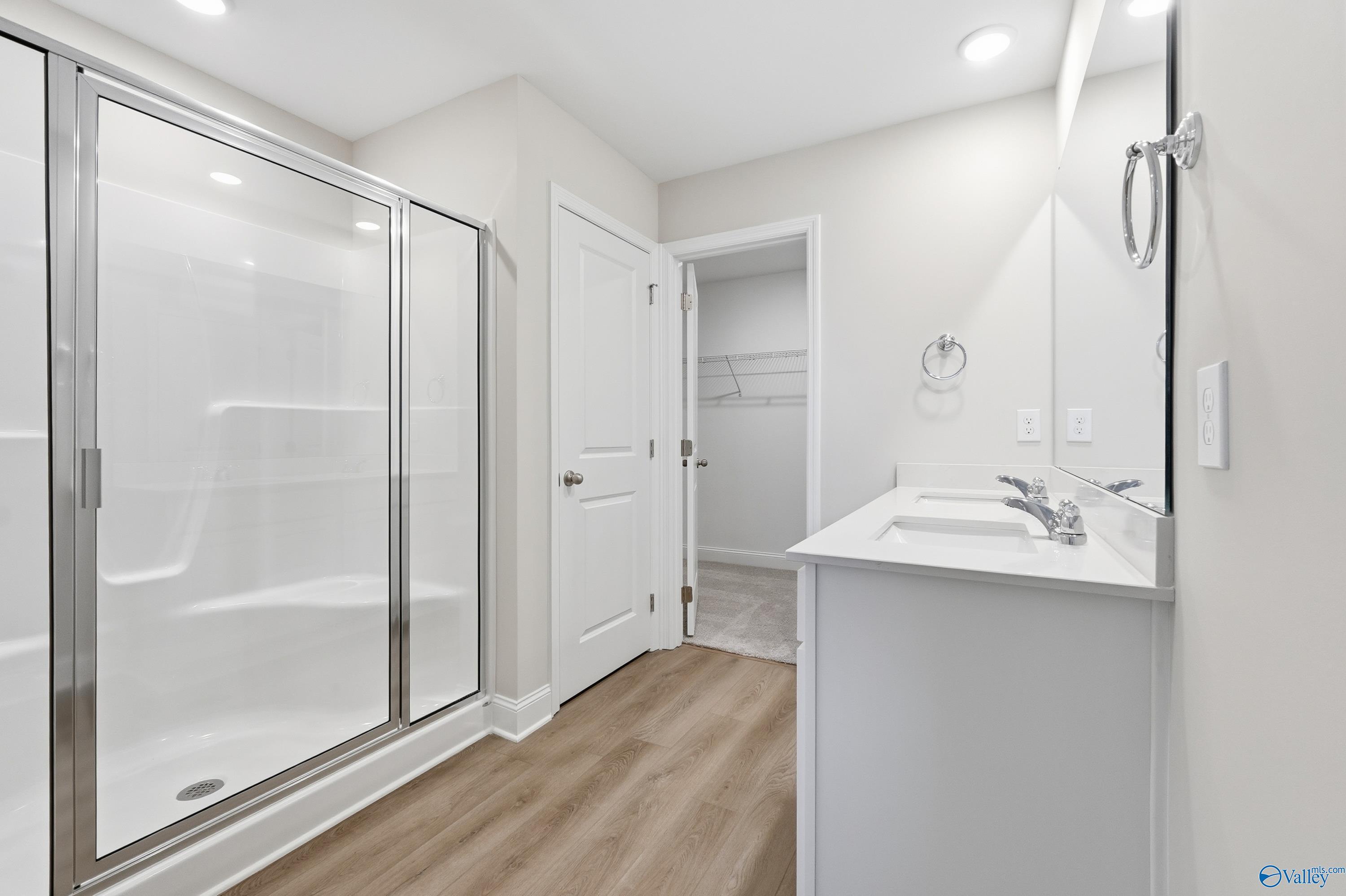 Modern master bathroom with frameless glass shower, white vanity sink, and walk-in closet door in Davidson Homes The Franklin, New Market, Alabama