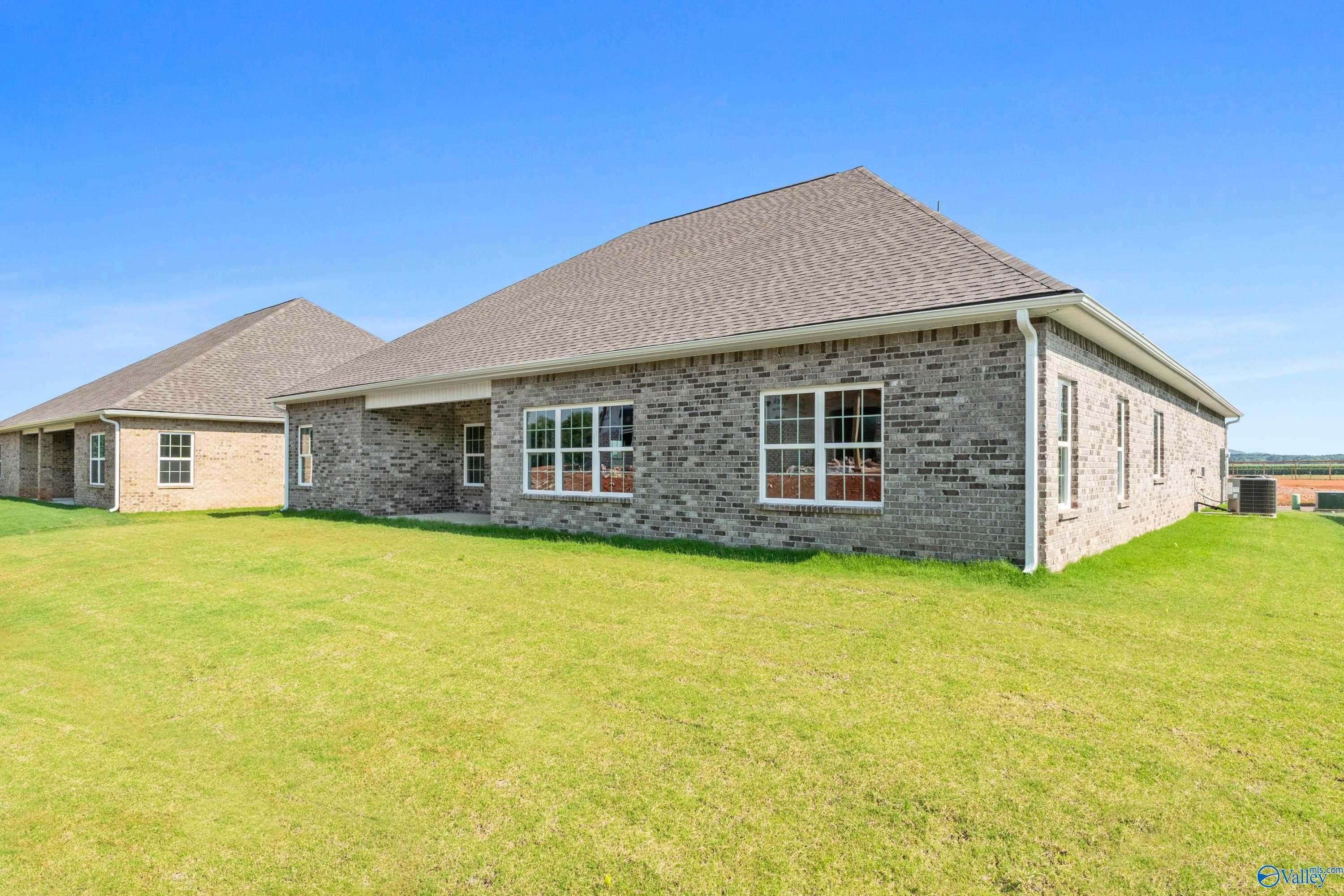 Single-story brick home with shingled roof, large windows, and lush green lawn in Kendall Farms, Toney, Alabama by Davidson Homes The Finleigh