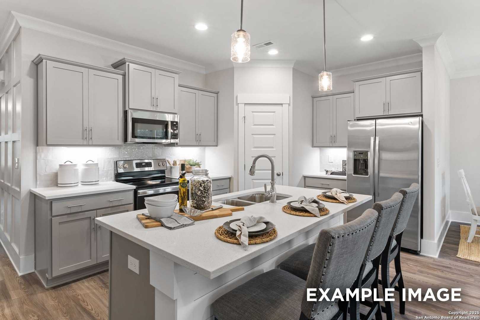 Modern kitchen featuring gray shaker cabinets, white quartz island with bar stools, stainless appliances in Davidson Homes The Daphne H, Seguin, TX