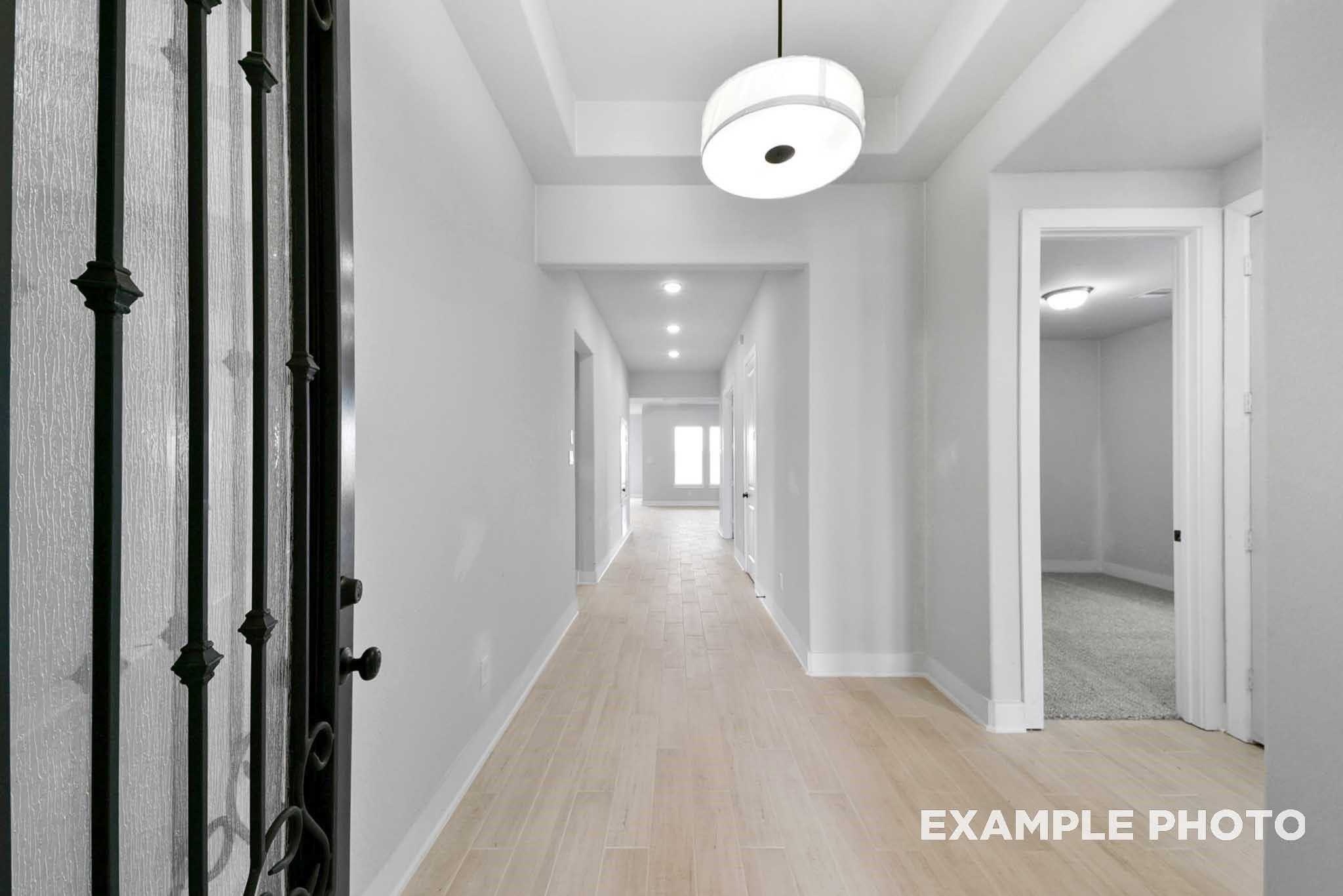 Grand entry hallway with wrought iron door, light wood floors, and recessed lighting in Davidson Homes The George A, Lago Mar, Texas City
