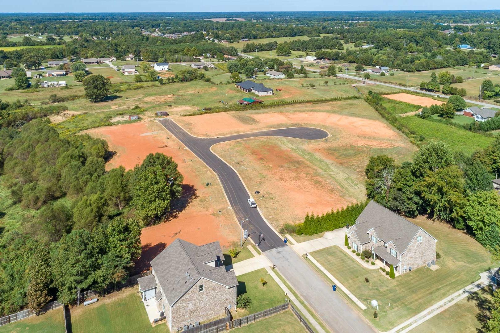 Aerial view of developing Little Burwell Estates in Harvest Alabama featuring new stone homes paved roads red clay lots and surrounding trees
