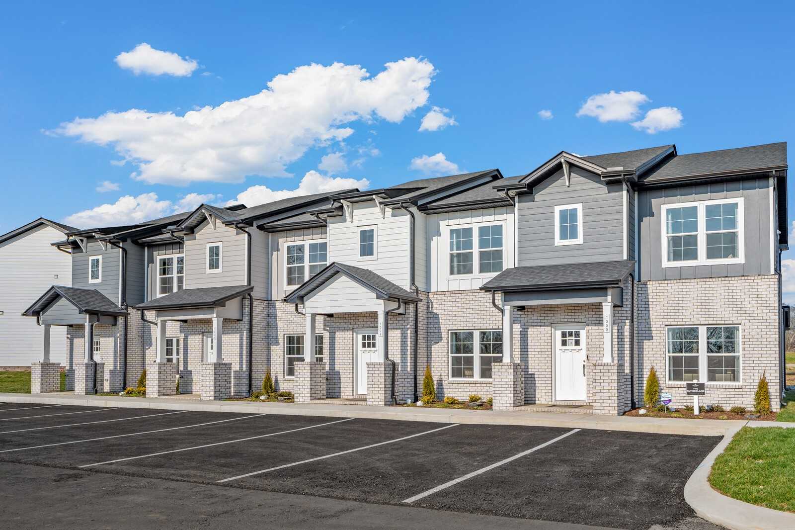Row of modern 2-story townhomes with gray siding, brick bases, and garages in The Towns at Red River, Gallatin, Tennessee by Davidson Homes