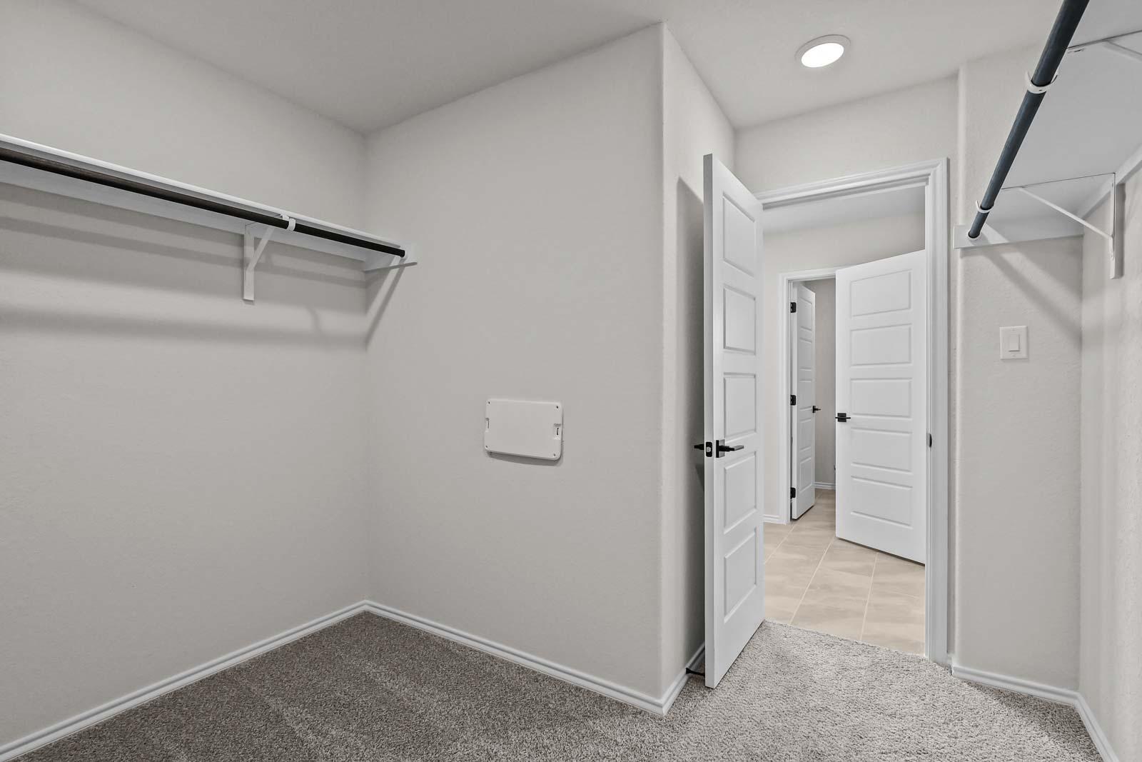 Spacious walk-in closet in The Florence B master suite featuring neutral carpeting, white shelving, and dual entry doors.