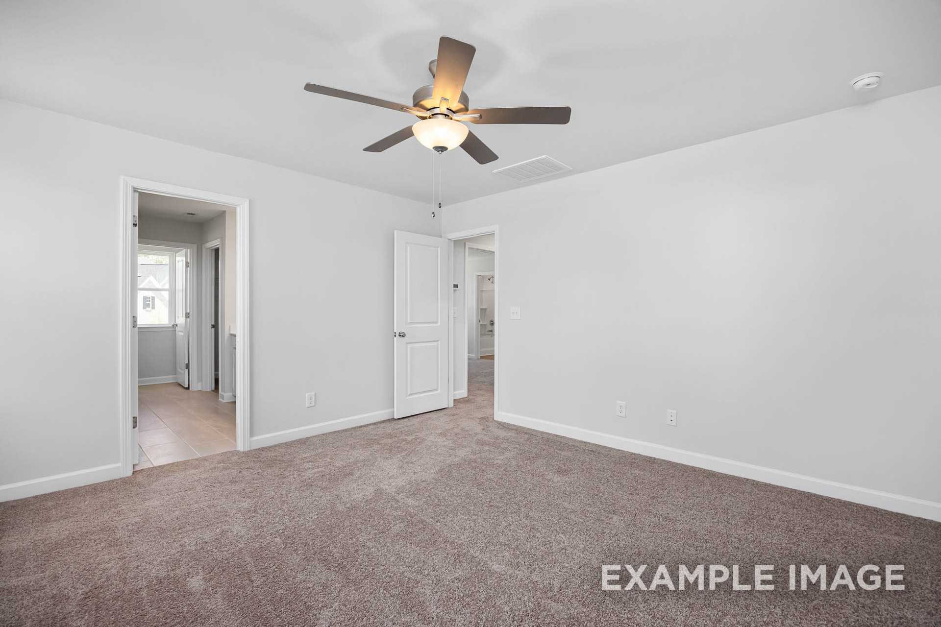 Spacious master bedroom in The Gavin C with light gray walls, carpeted floor, ceiling fan, and ensuite doorways