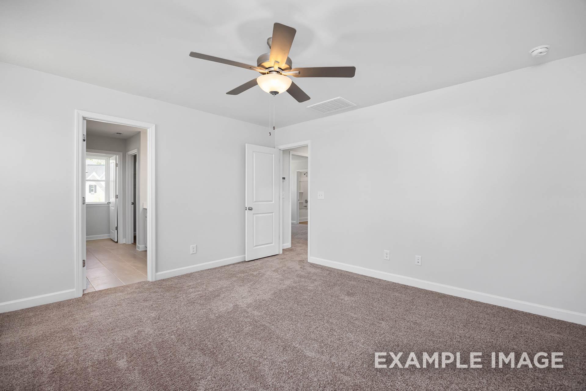 Spacious master bedroom in The Gavin B with light gray walls, beige carpet, ceiling fan, and ensuite bath access