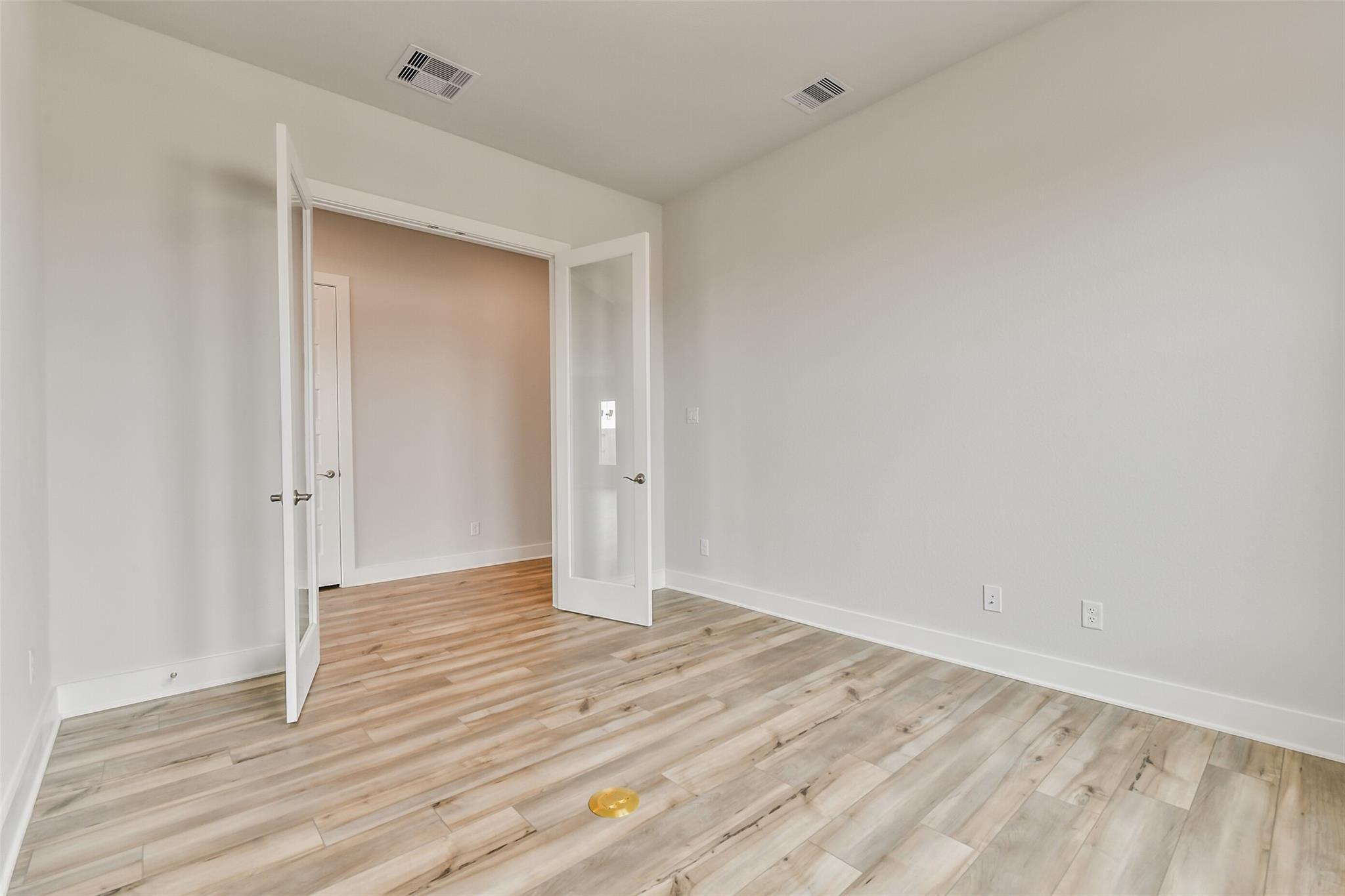 Empty study room with open French doors, light wood flooring, and neutral walls in Davidson Homes The George A, Lago Mar, Texas City