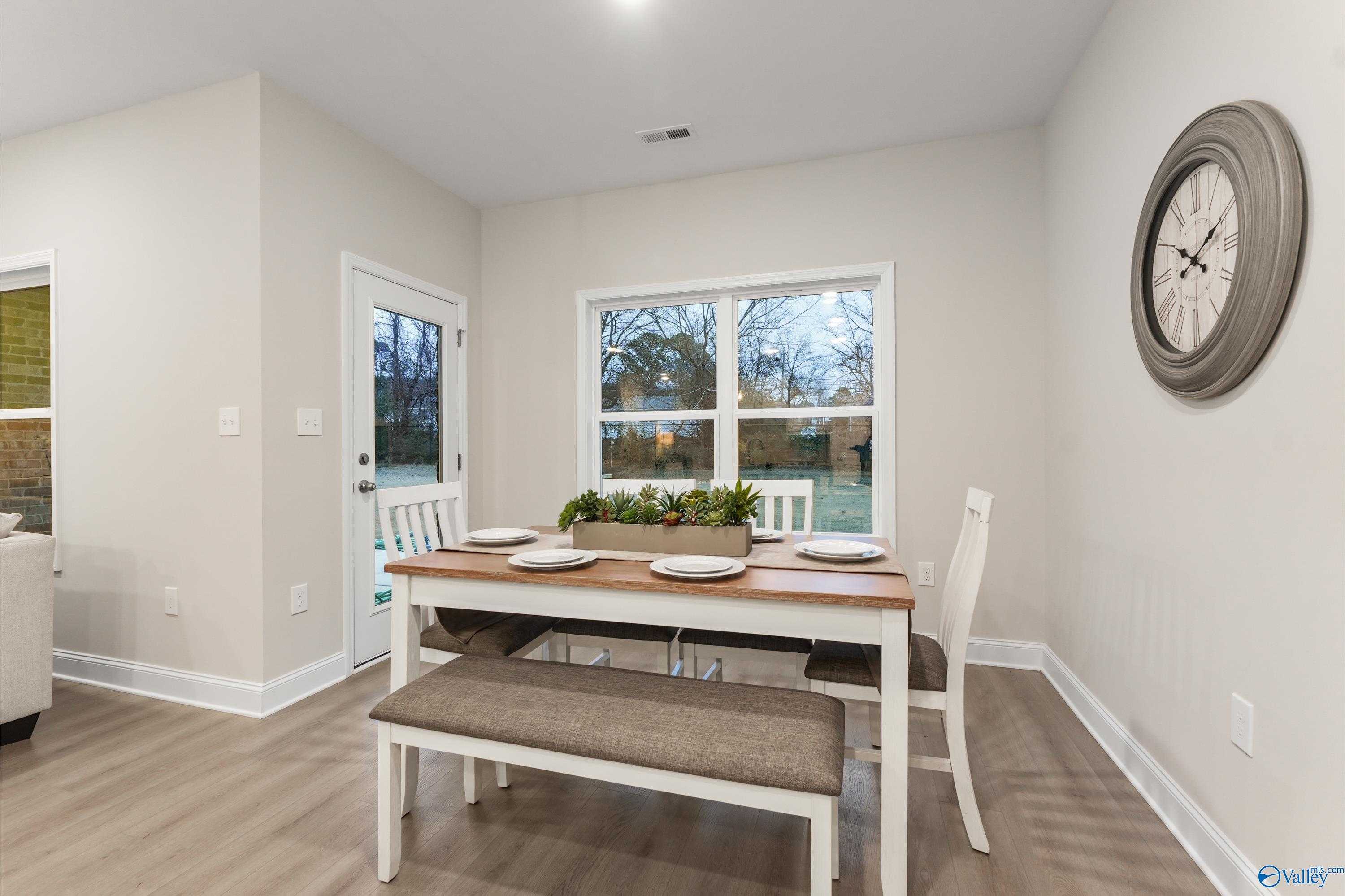 Cozy dining nook with wooden table, white chairs, bench, and plant centerpiece in The Asheville C, Davidson Homes, Jaguar Hills, Huntsville, Alabama