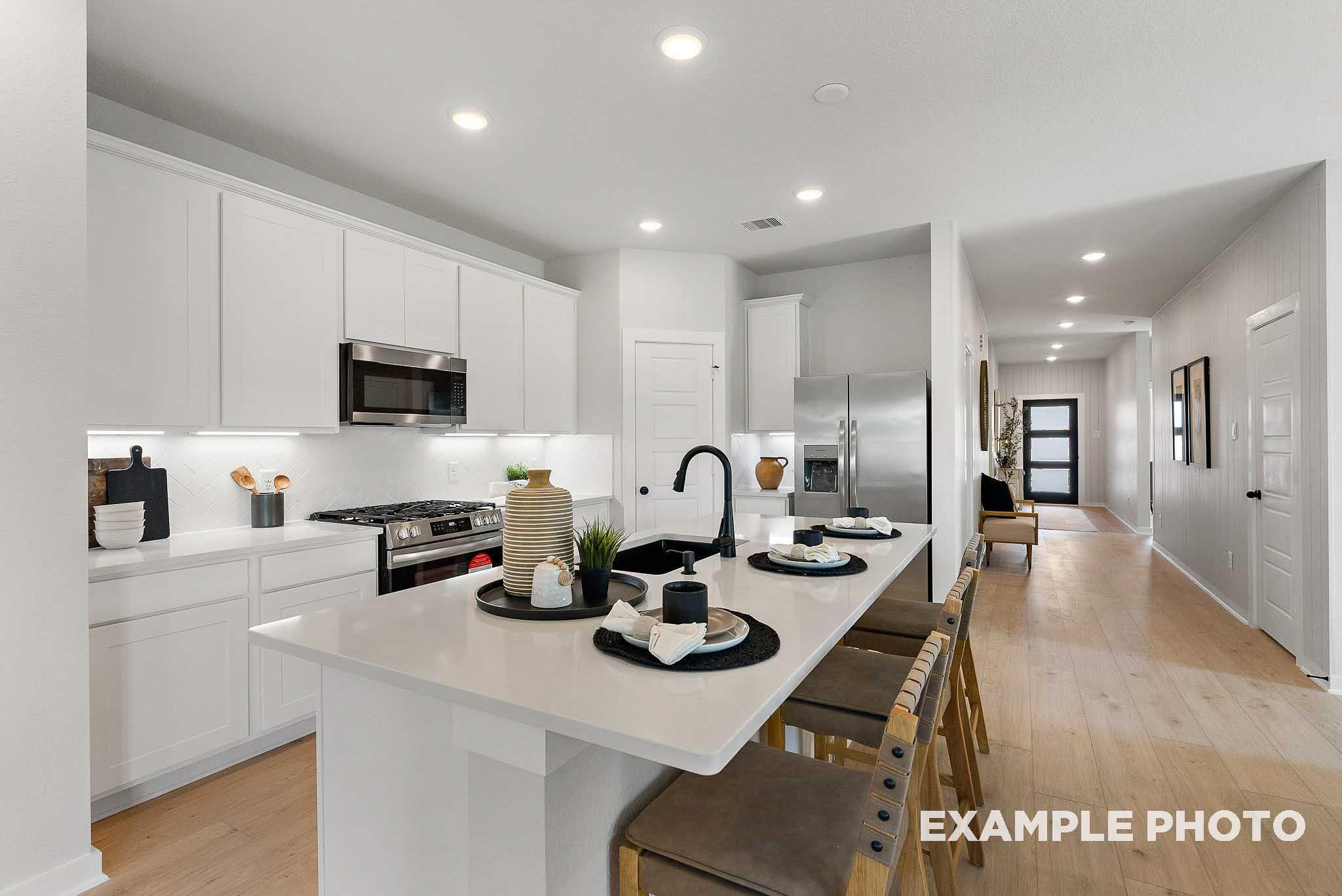 Modern kitchen with white cabinets, quartz island, and stainless appliances in The Everett E floor plan, Crosby, Texas.