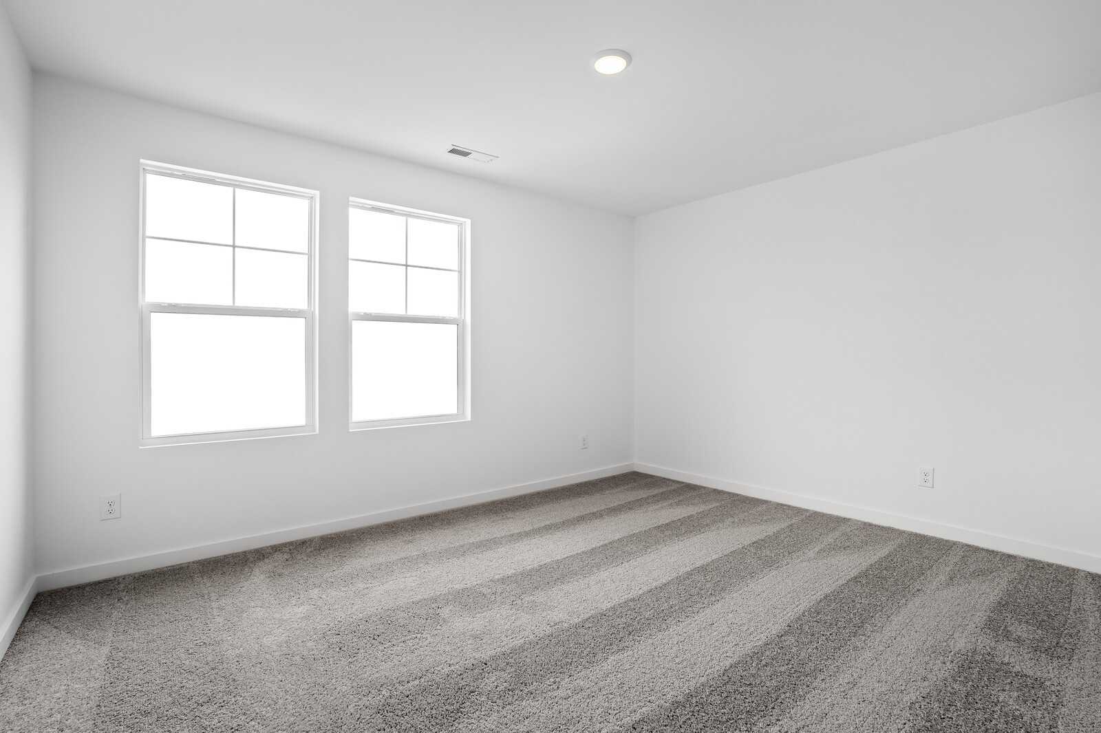 Bright secondary bedroom with double windows and neutral striped carpet in Davidson Homes The Logan C, White House, TN