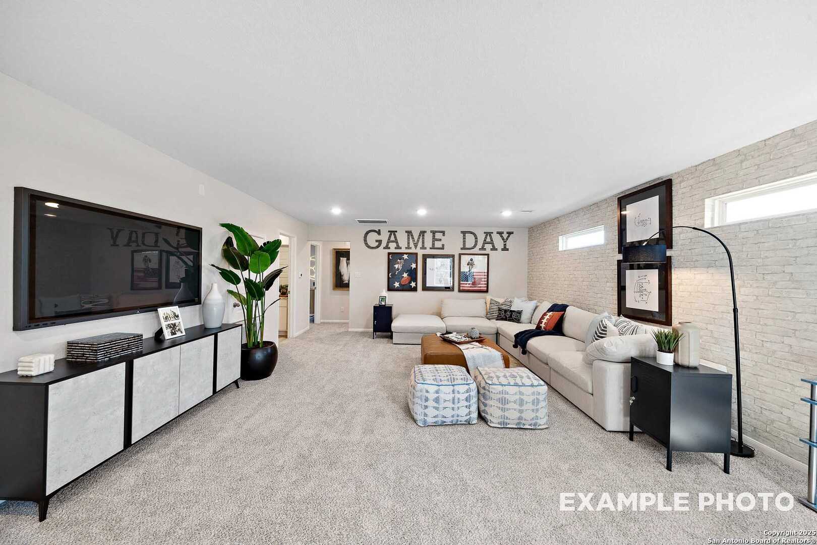 Cozy game room featuring large wall TV, sectional sofa, GAME DAY wall decor, and plants in Davidson Homes The San Marcos D, San Antonio