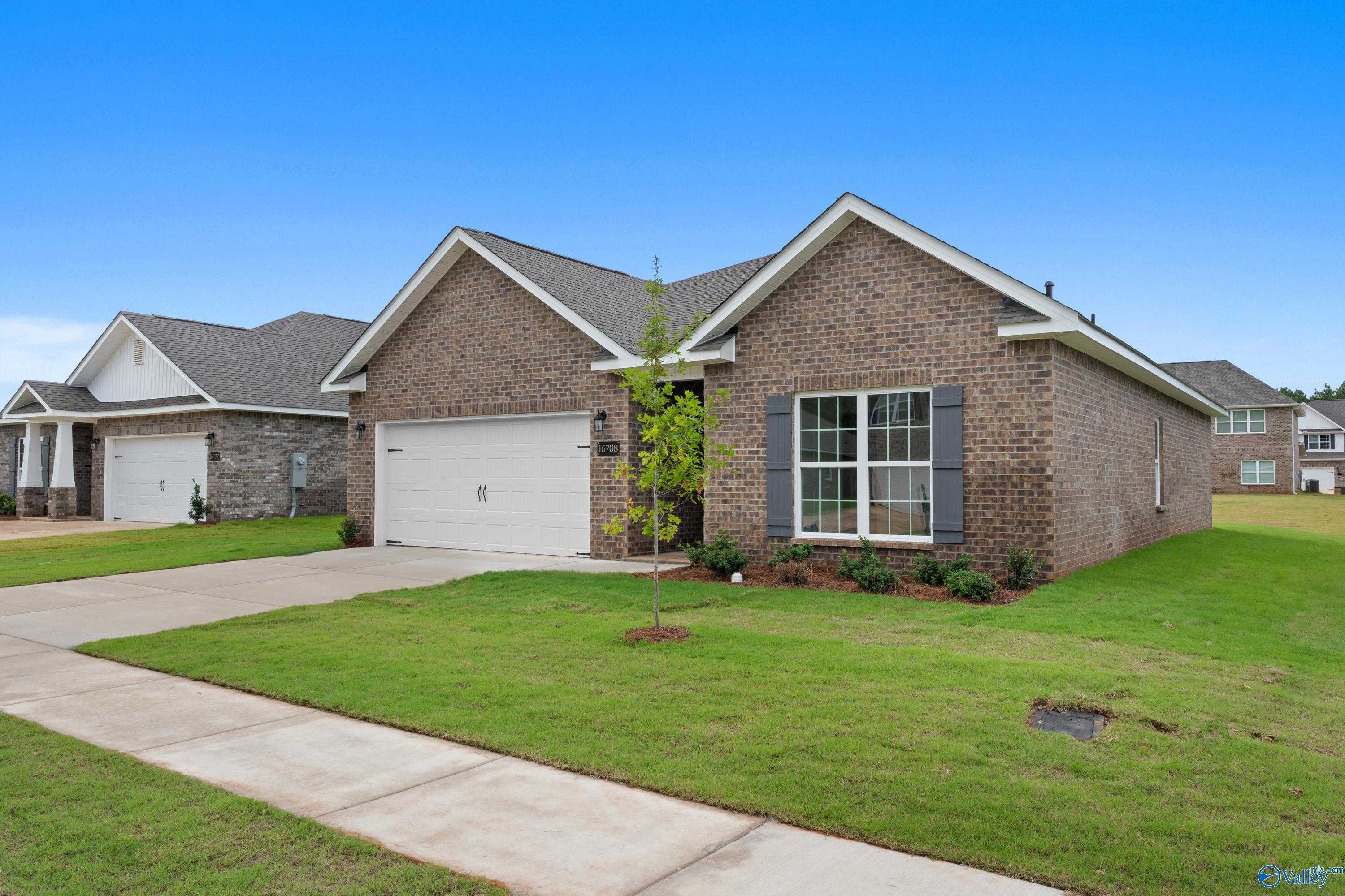 Charming brick 1-story home with 2-car garage, driveway, young tree, and lush lawn in Ricketts Farm, Athens, Alabama