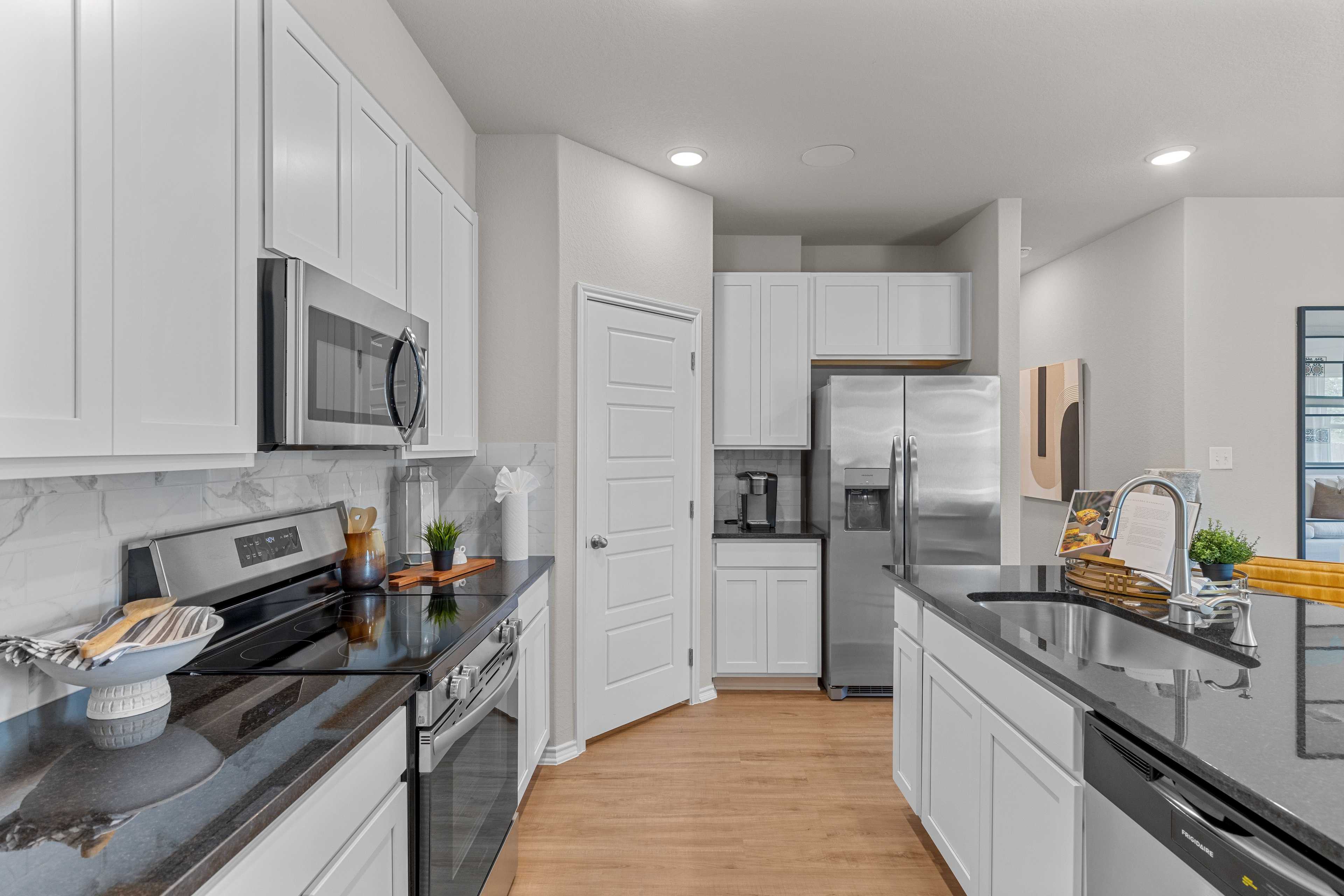 Modern kitchen with white shaker cabinets, black quartz counters, stainless appliances, and hardwood floors at Meadows at Oak Creek San Antonio