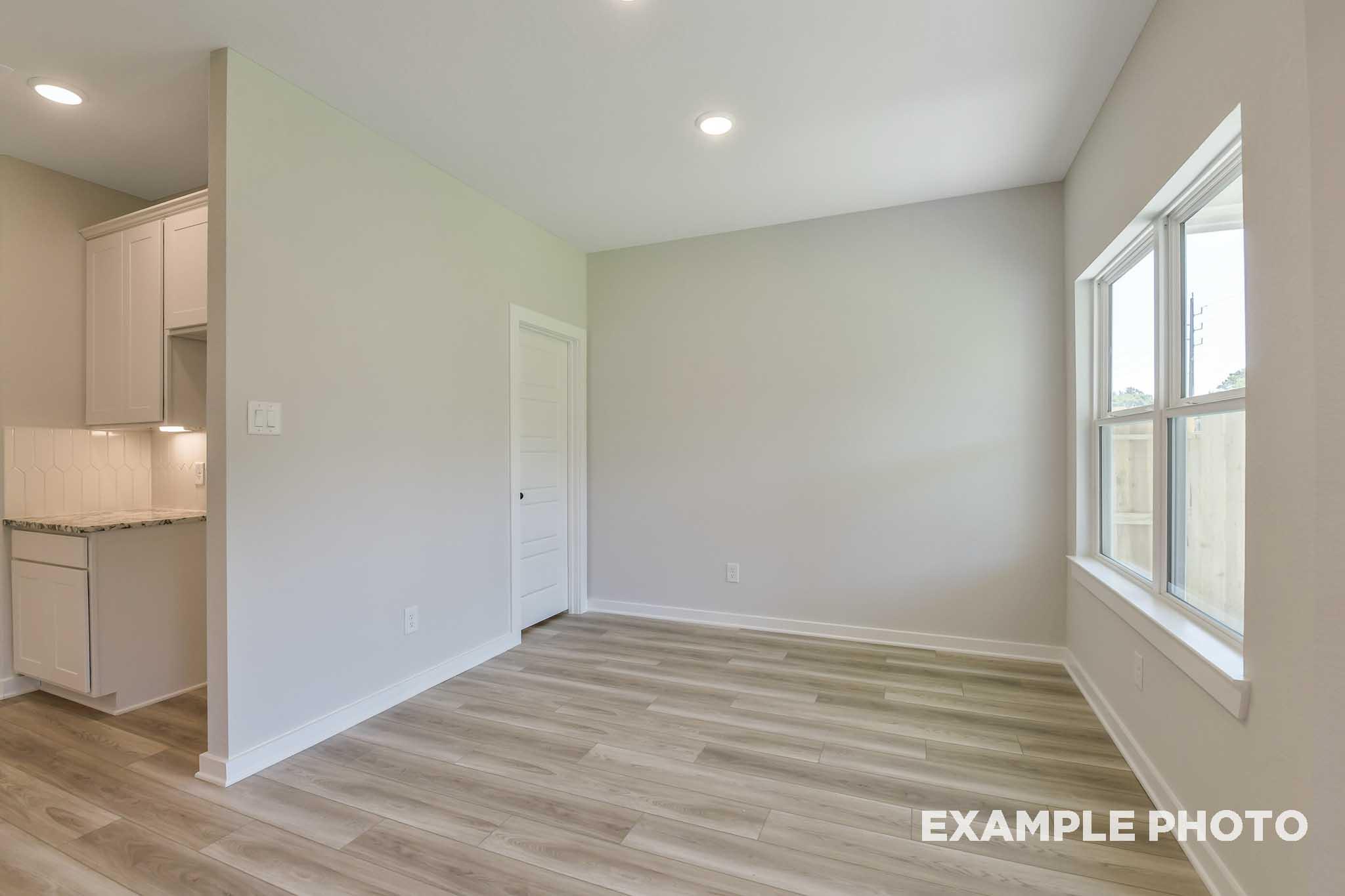 Spacious laundry room in The Daphne G home design with white cabinets, sink, light gray walls, and wood flooring