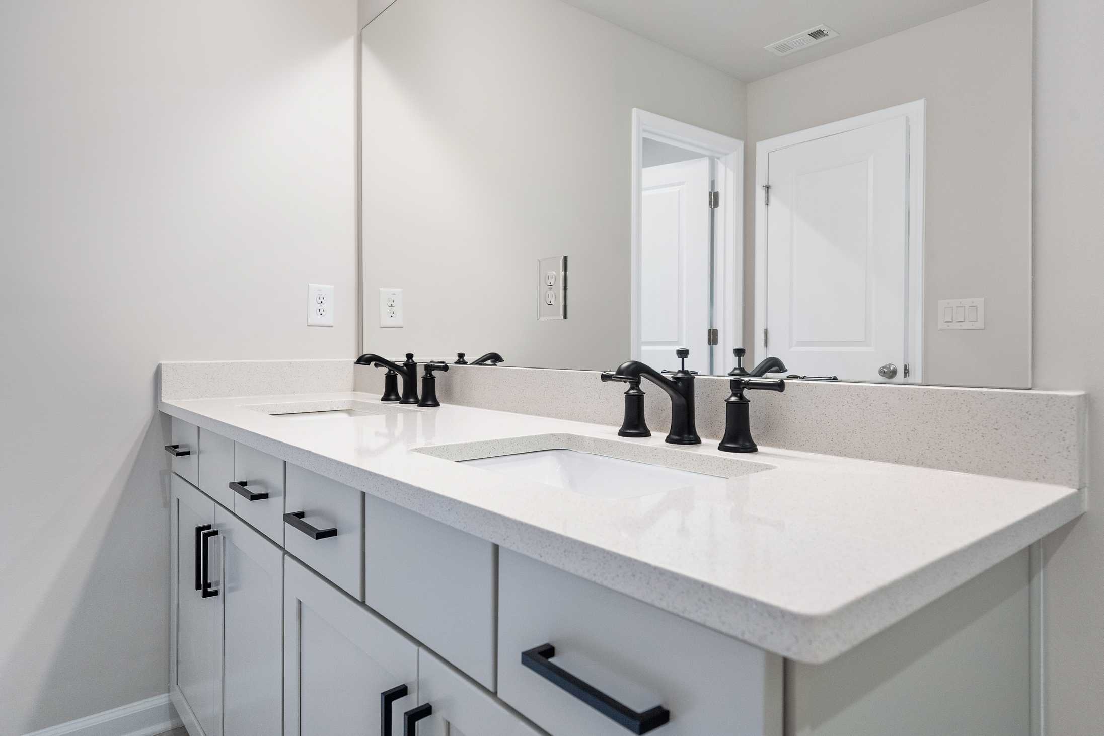 Modern double vanity in The Cary B master bathroom featuring quartz countertop, black faucets, and shaker cabinets