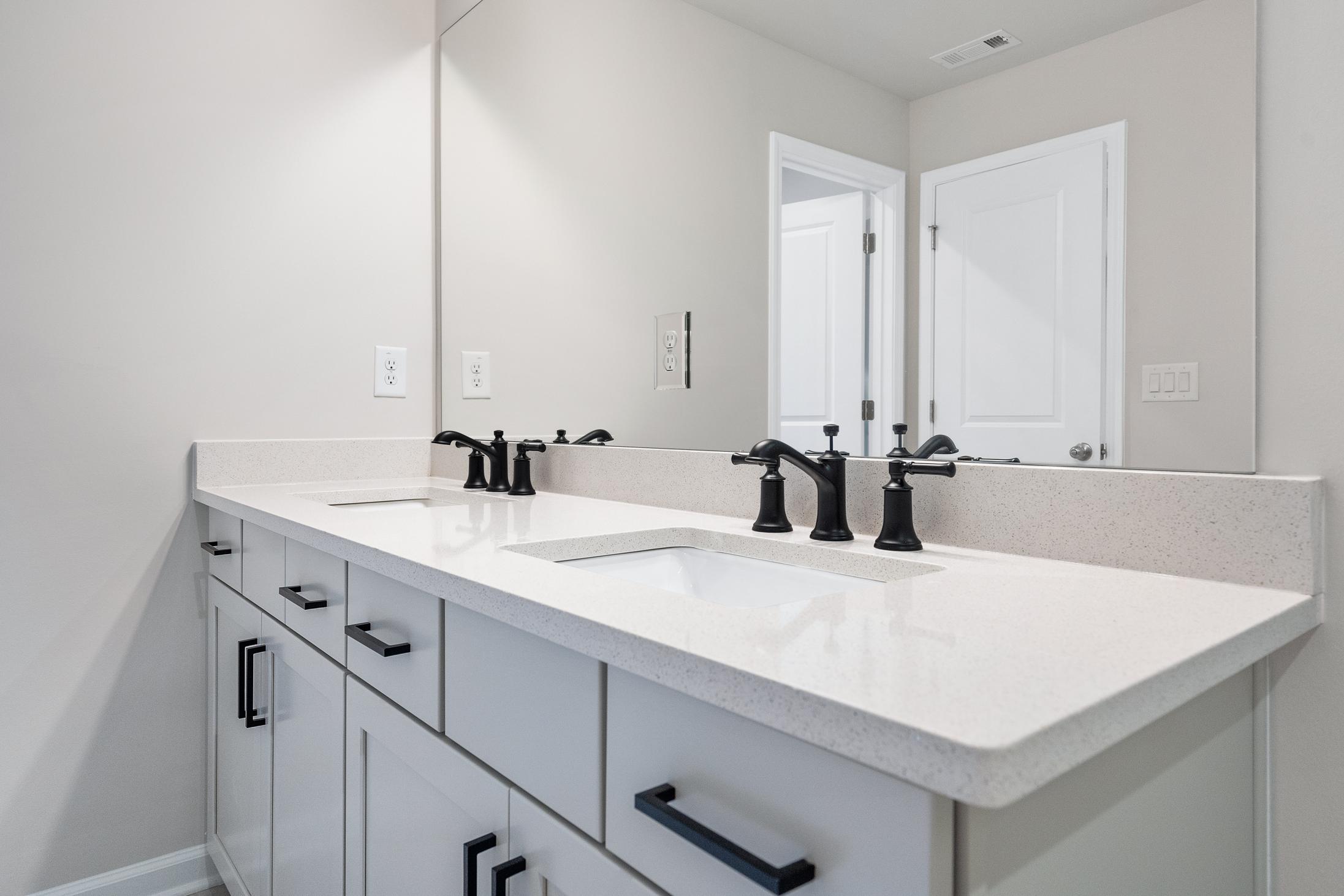 Modern double vanity in The Cary B master bathroom featuring quartz countertop, black faucets, and shaker cabinets