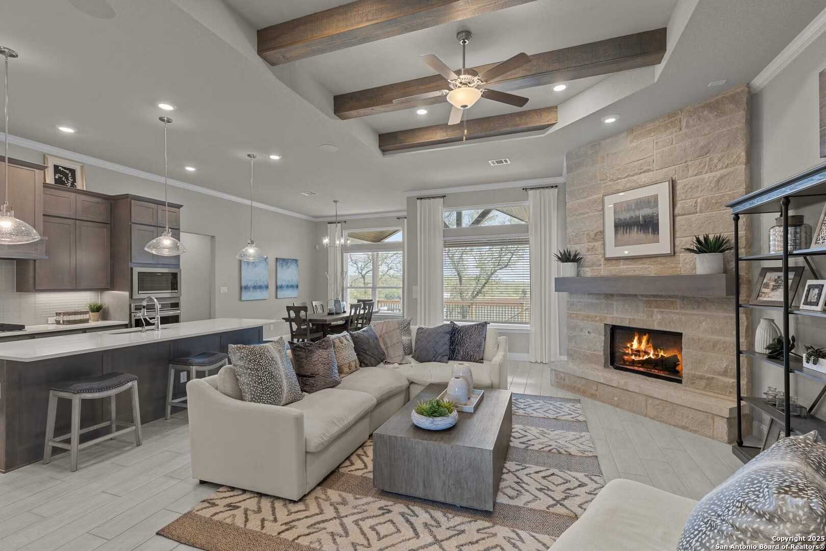 Open-concept living and kitchen with beamed ceiling, stone fireplace, and large windows in Davidson Homes The Garner A, Castroville, Texas