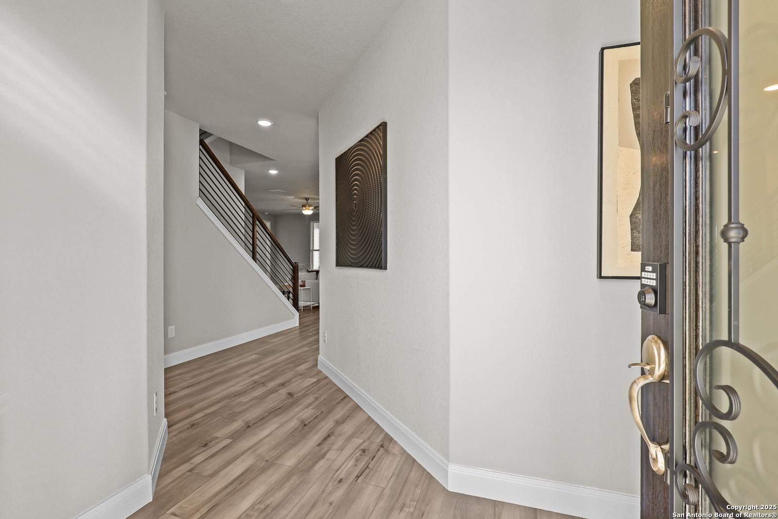 Welcoming entry foyer with sweeping staircase, white walls, and hardwood floors in The Jennings G 5-bedroom home, Castroville, Texas