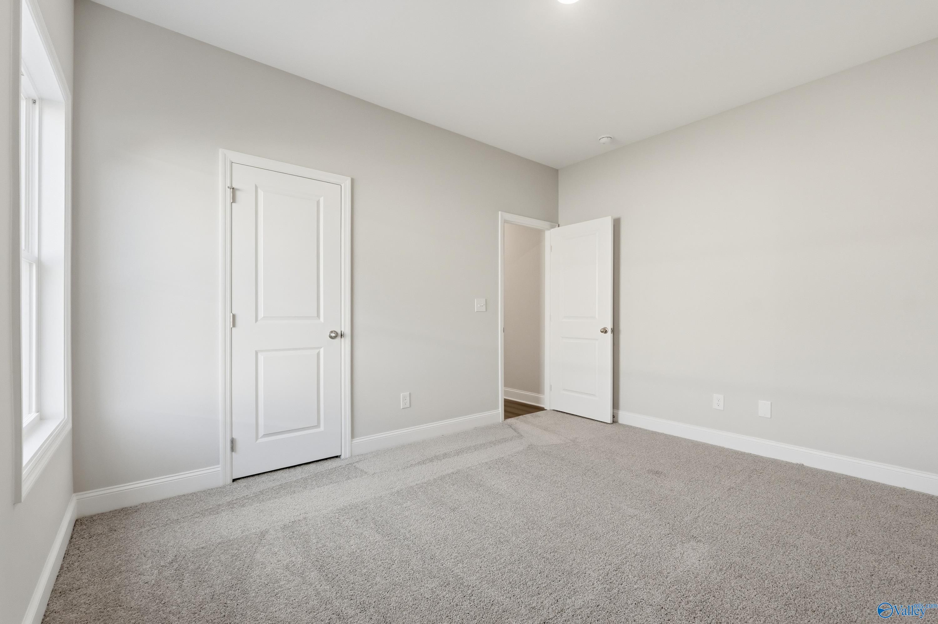 Bright secondary bedroom with neutral gray walls, plush carpet, and adjacent bath door in Davidson Homes The Daphne C, Arab, Alabama